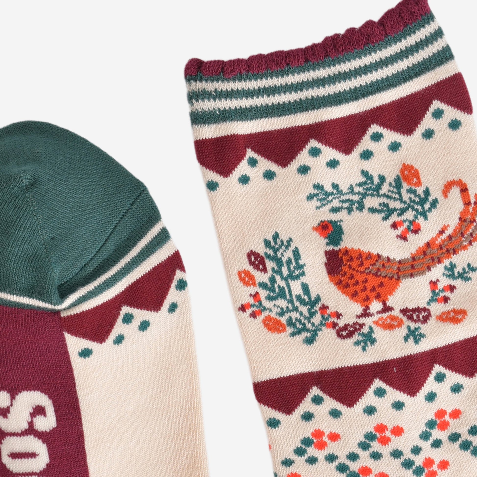 close up of the toe and cuff of the socks, the toe is green with a cream striped outline, the cuff is scalloped with a burgundy edge and green and cream striped pattern