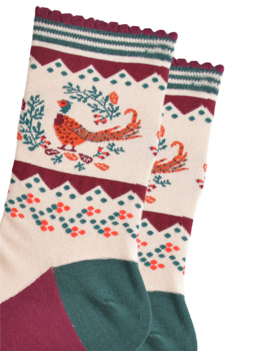 close up of the woodland pheasant and autumnal wreath on the ankle of the socks, the pheasants are stranding in the middle of a green horseshoe shaped wreath, there are orange and red fallen leaves scattered around