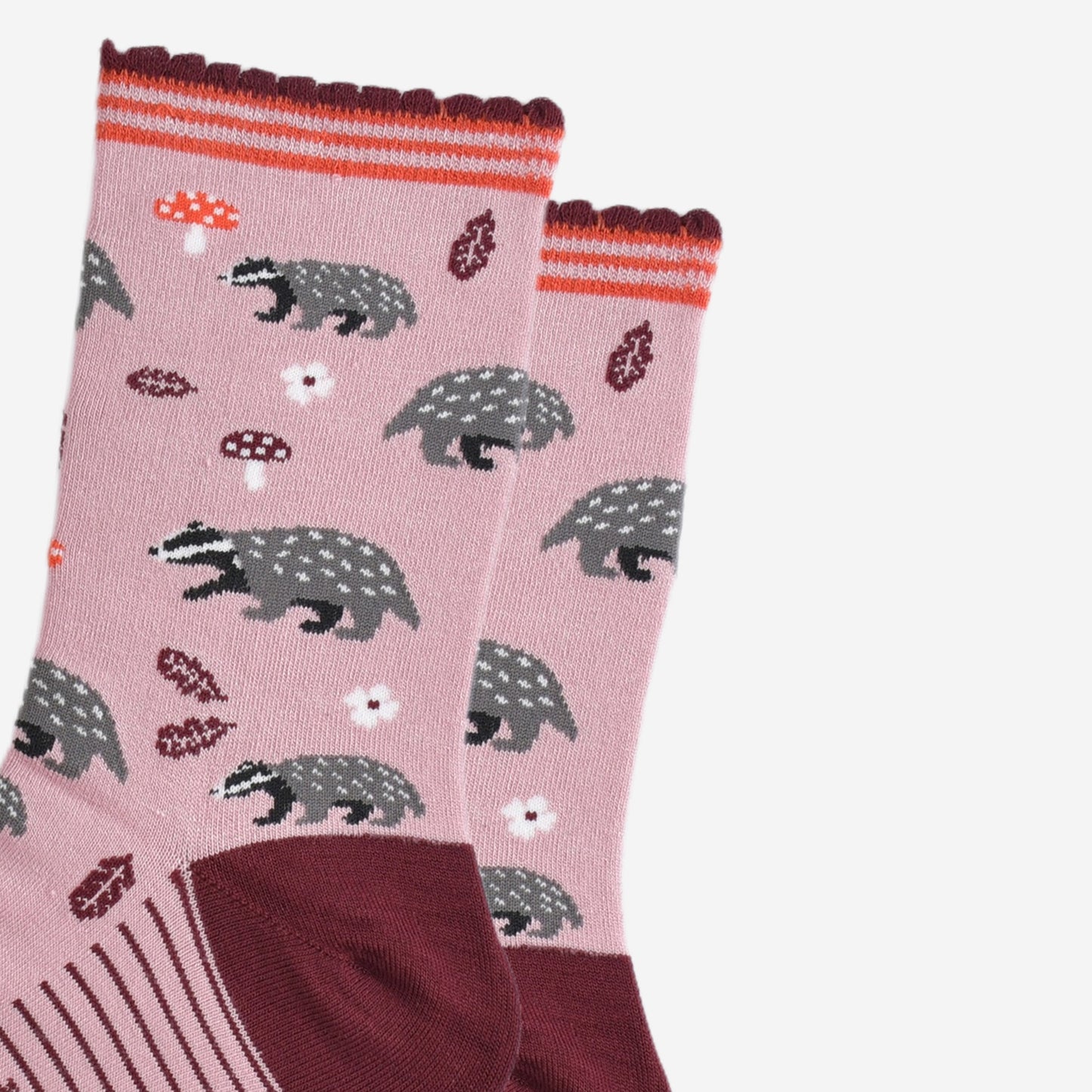 close up of the woodland badger pattern, the socks have grey and black badgers, red toadstools, burgundy red leaves and white flowers on them