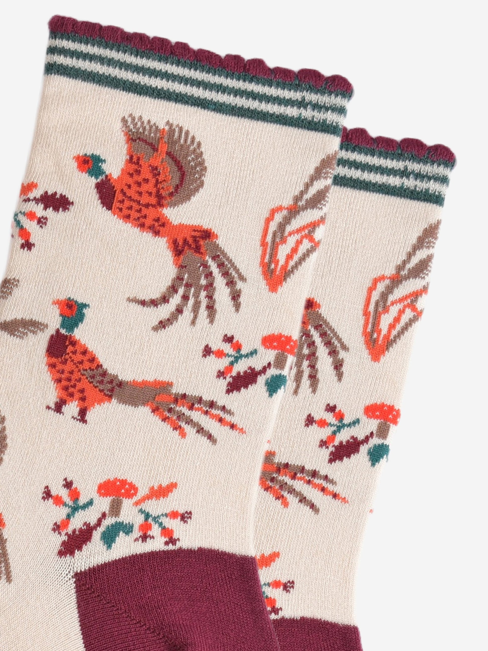 close up of the pheasants, they are illustrated in orange and red and appear to be walking and flying, surrounding the pheasants are autumn leaves and red toadstools