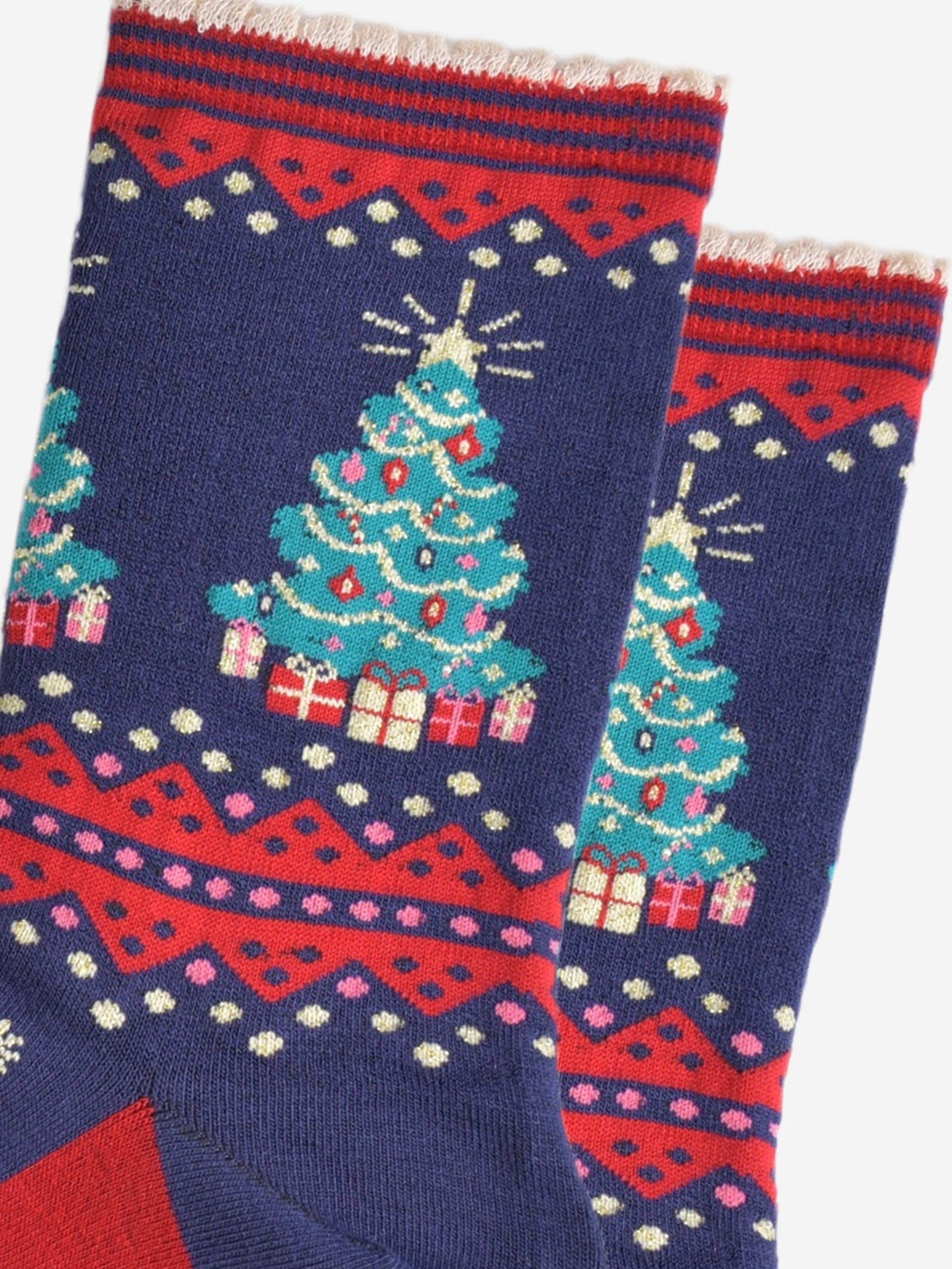 close up of the christmas tree design on the ankle of the socks, the tree is green with multicoloured baubles, gold tinsel and red candy canes. below the tree are wrapped gifts 