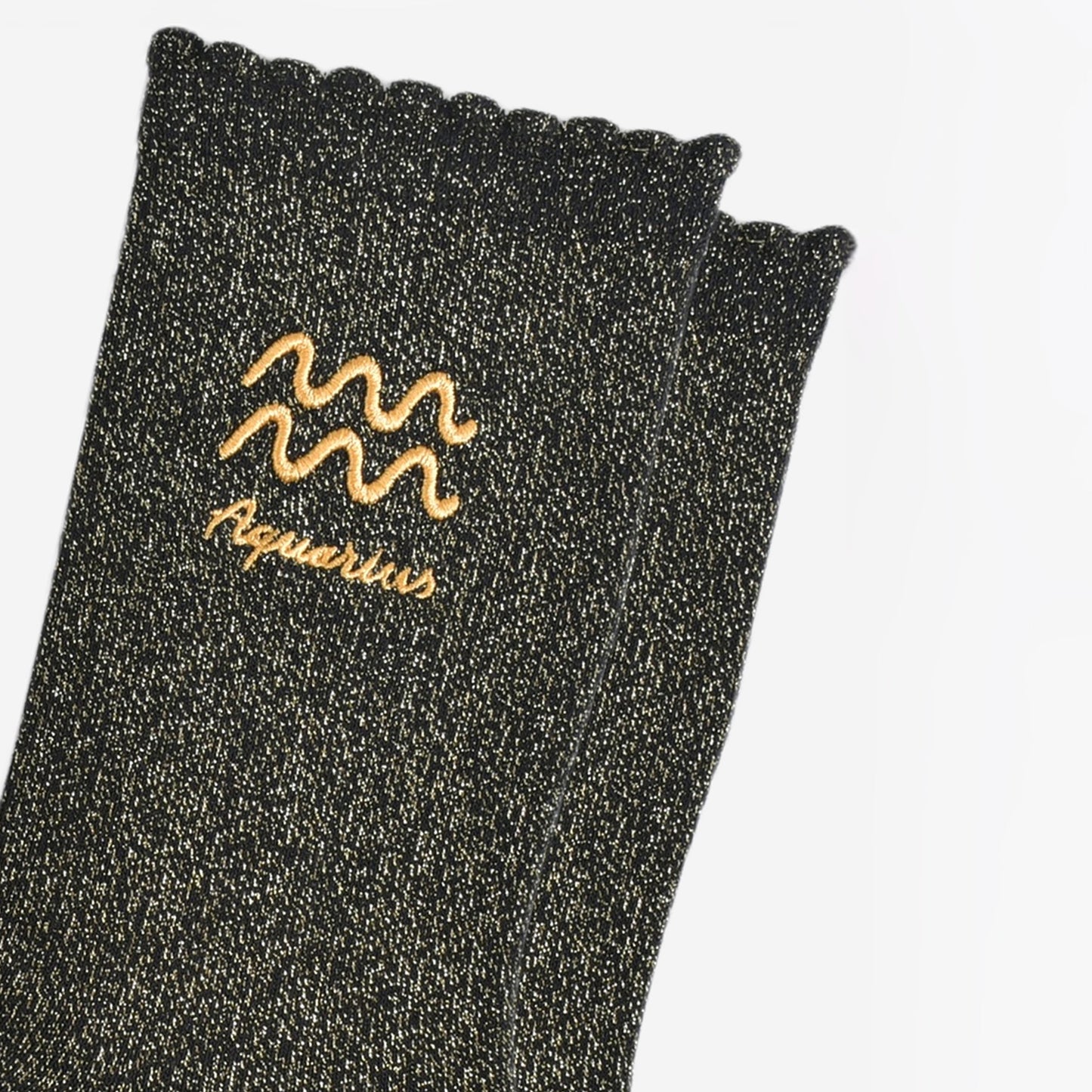 close up of the gold embroidered zodiac detail on the ankle of the socks, showing clearly the symbol of and word aquarius