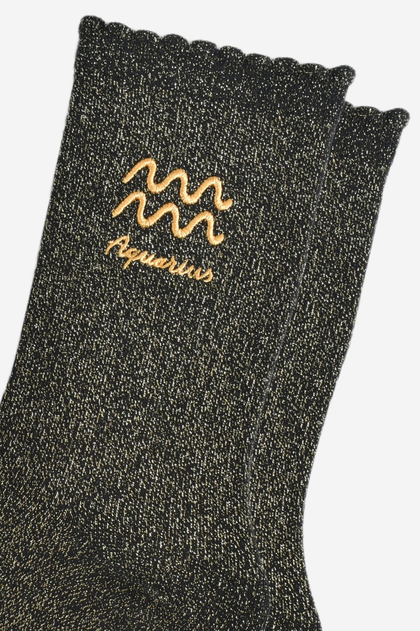 close up of the gold embroidered zodiac detail on the ankle of the socks, showing clearly the symbol of and word aquarius