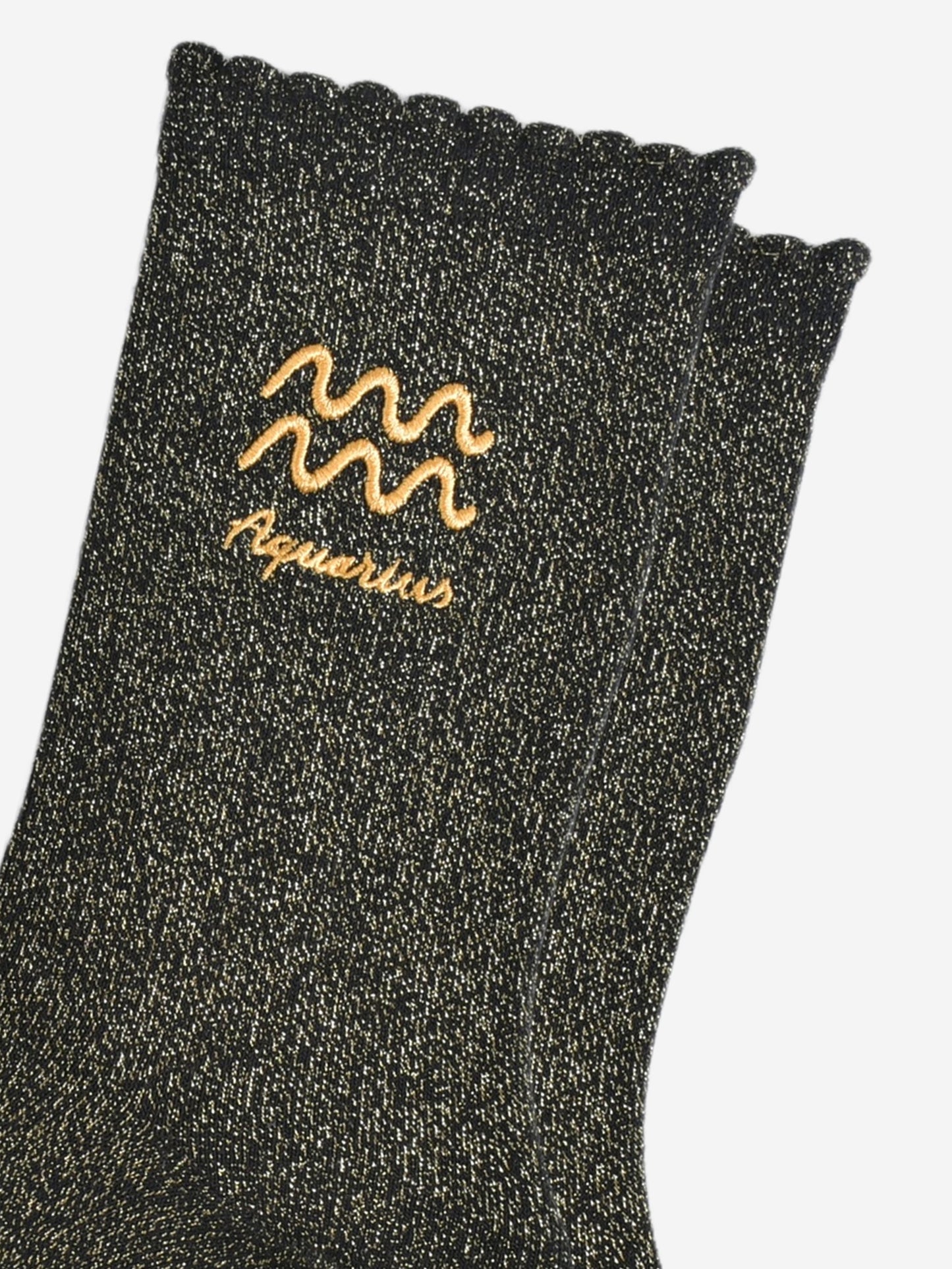 close up of the gold embroidered zodiac detail on the ankle of the socks, showing clearly the symbol of and word aquarius