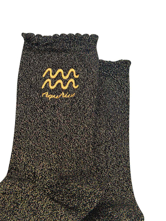 close up of the gold embroidered zodiac detail on the ankle of the socks, showing clearly the symbol of and word aquarius
