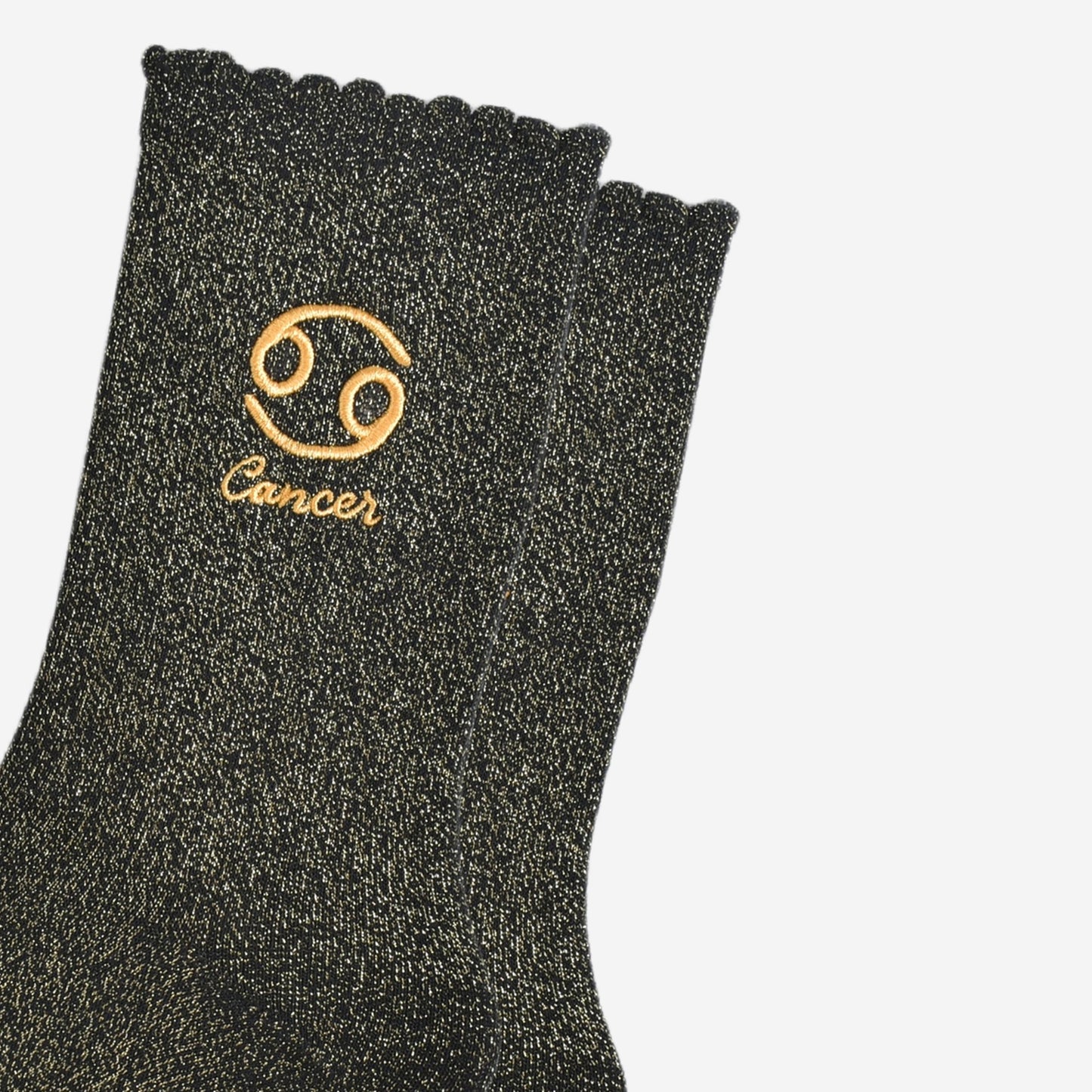 close up of the gold embroidered zodiac detail on the ankle of the socks, showing clearly the symbol of and word cancer