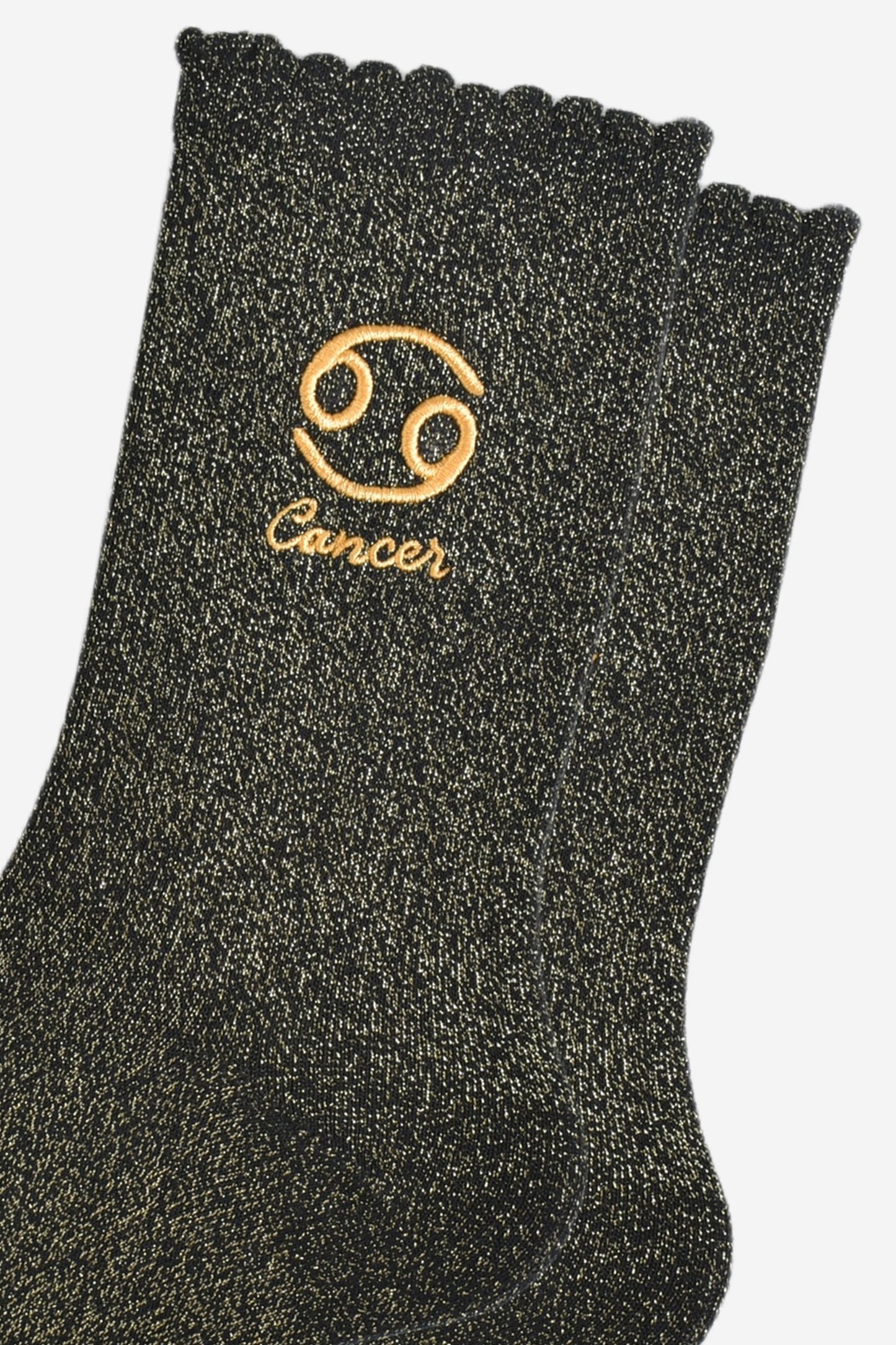 close up of the gold embroidered zodiac detail on the ankle of the socks, showing clearly the symbol of and word cancer