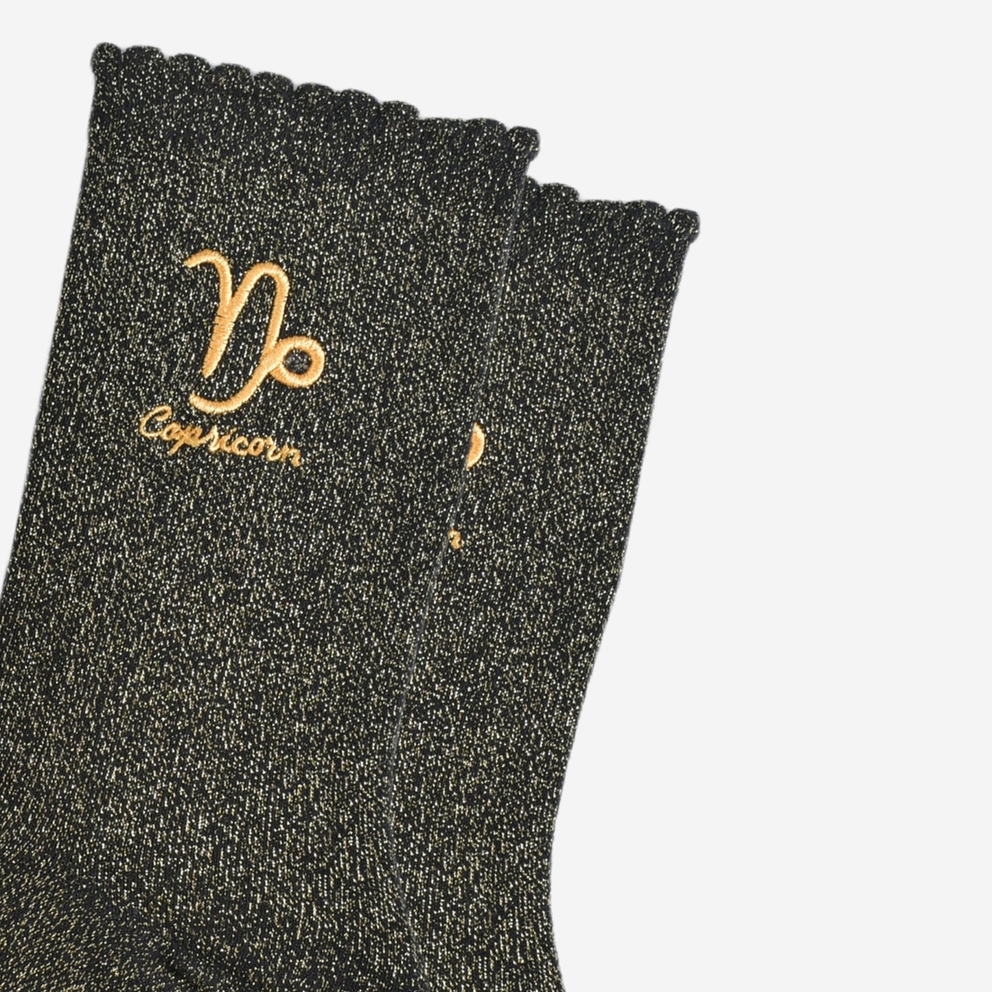 close up of the gold embroidered zodiac detail on the ankle of the socks, showing clearly the symbol of and word capricorn