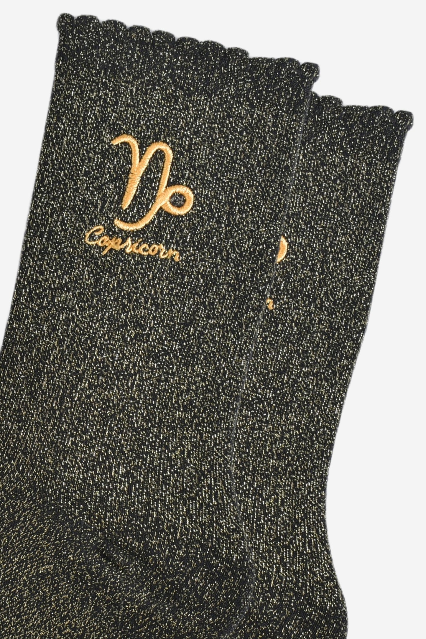 close up of the gold embroidered zodiac detail on the ankle of the socks, showing clearly the symbol of and word capricorn