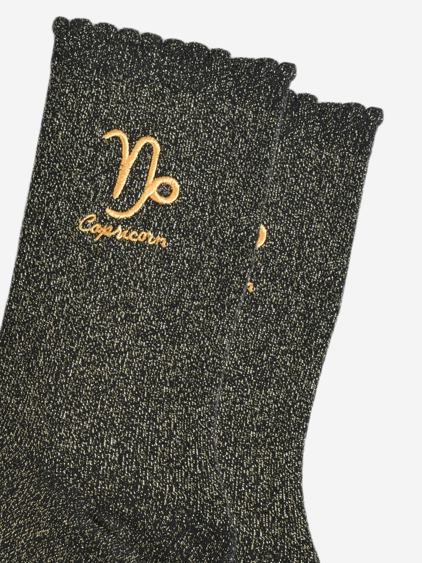 close up of the gold embroidered zodiac detail on the ankle of the socks, showing clearly the symbol of and word capricorn