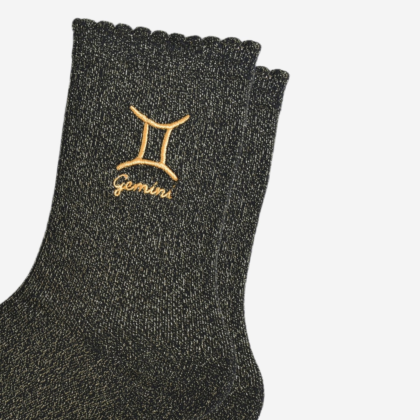 close up of the gold embroidered zodiac detail on the ankle of the socks, showing clearly the symbol of and word gemini