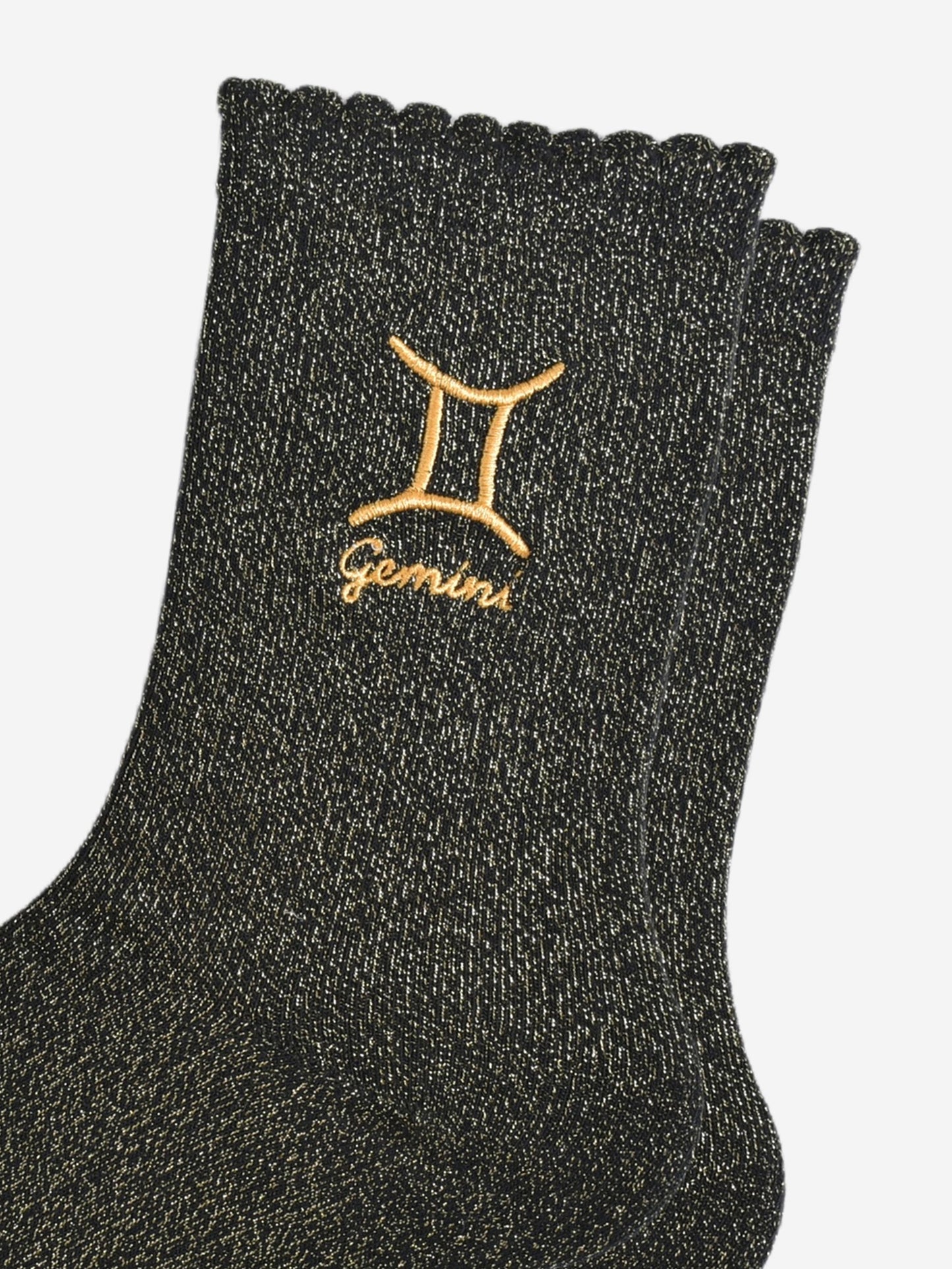 close up of the gold embroidered zodiac detail on the ankle of the socks, showing clearly the symbol of and word gemini