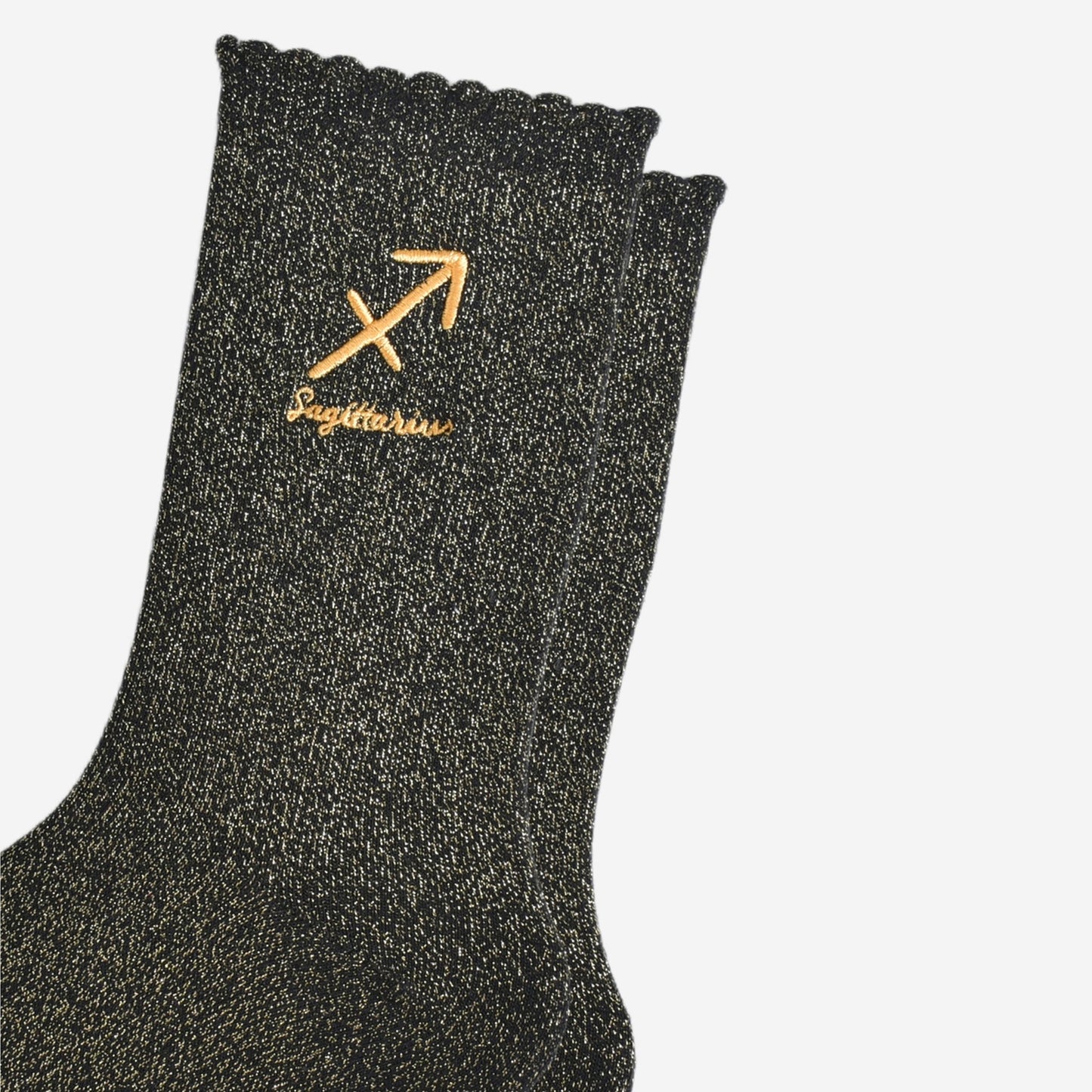 close up of the gold embroidered zodiac detail on the ankle of the socks, showing clearly the symbol of and word sagittarius