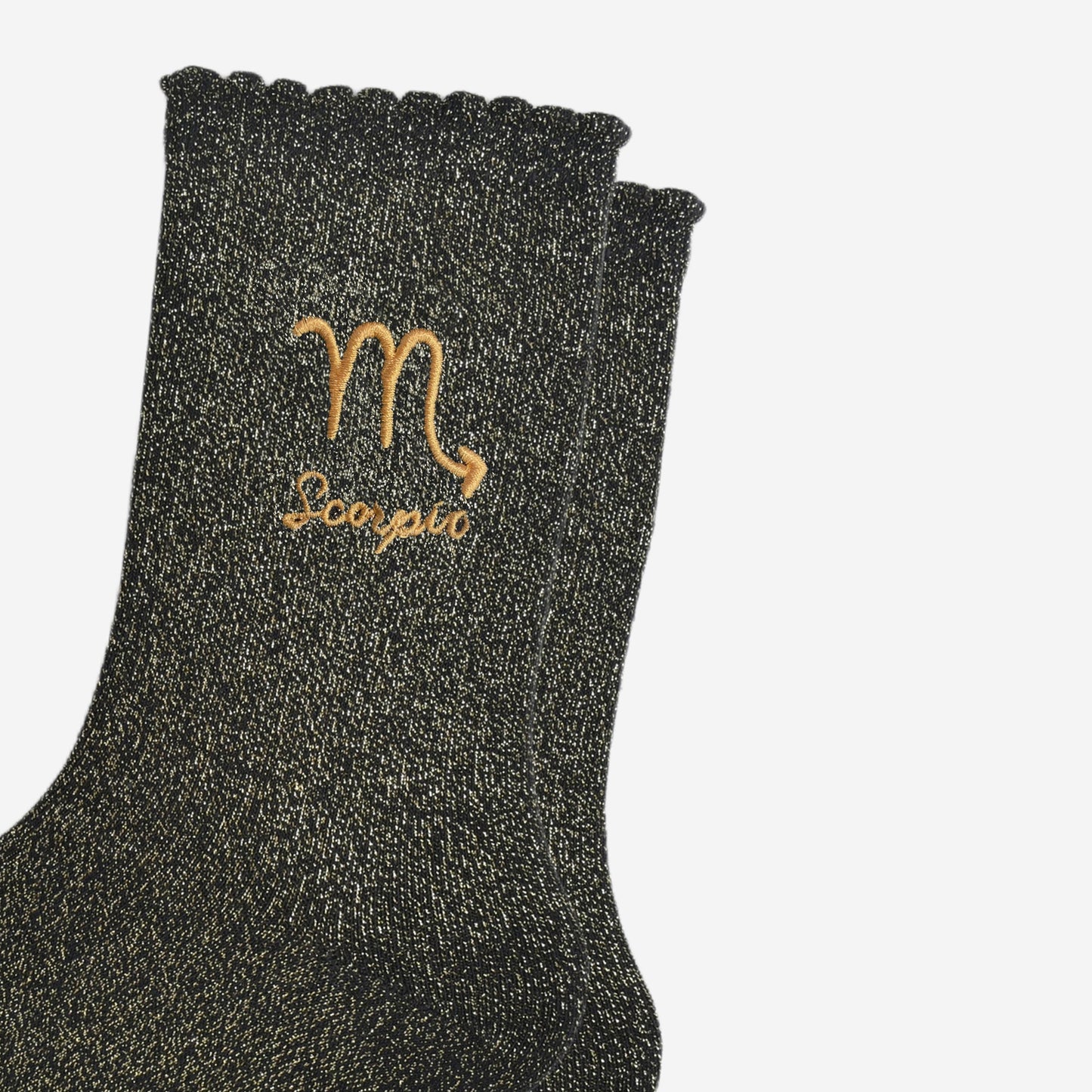 close up of the gold embroidered zodiac detail on the ankle of the socks, showing clearly the symbol of and word scorpio