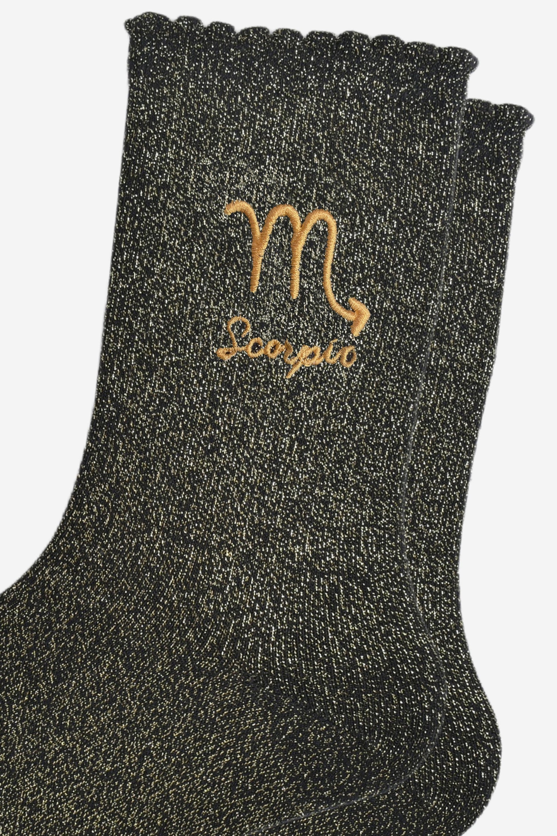 close up of the gold embroidered zodiac detail on the ankle of the socks, showing clearly the symbol of and word scorpio