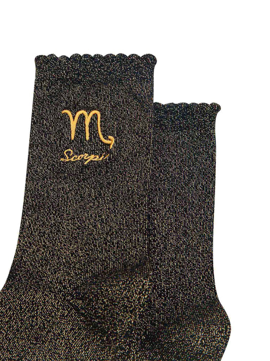 close up of the gold embroidered zodiac detail on the ankle of the socks, showing clearly the symbol of and word scorpio