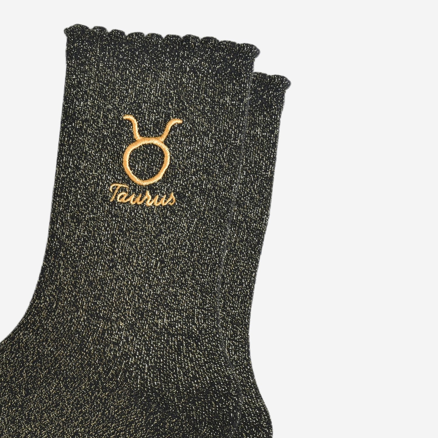 close up of the gold embroidered zodiac detail on the ankle of the socks, showing clearly the symbol of and word taurus