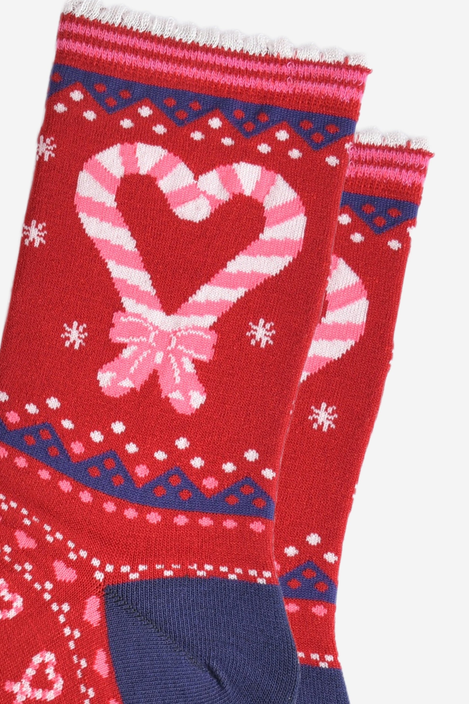 close up of the candy cane heart design on the ankle of the socks, there are two candy canes crossed at the bottom, making a love heart shape, they are pink and white striped on a red background