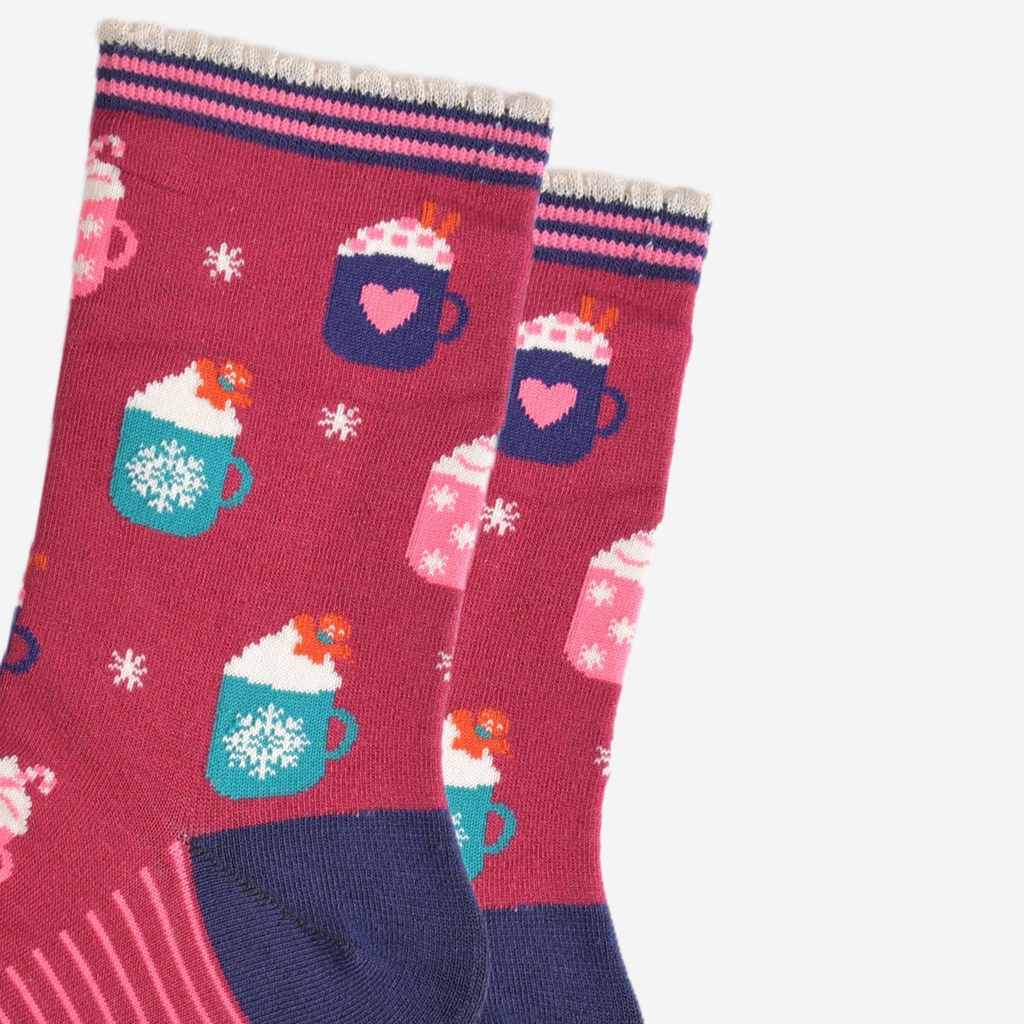 close up of the hot drinks design on the socks, there are teal coloured mugs with a white snowflake pattern topped with whipped creme and a gingerbread man cookie, there are pink mugs with pink candy canes and navy mugs with pink love hearts with pink sugar hearts and cinnamon sticks.