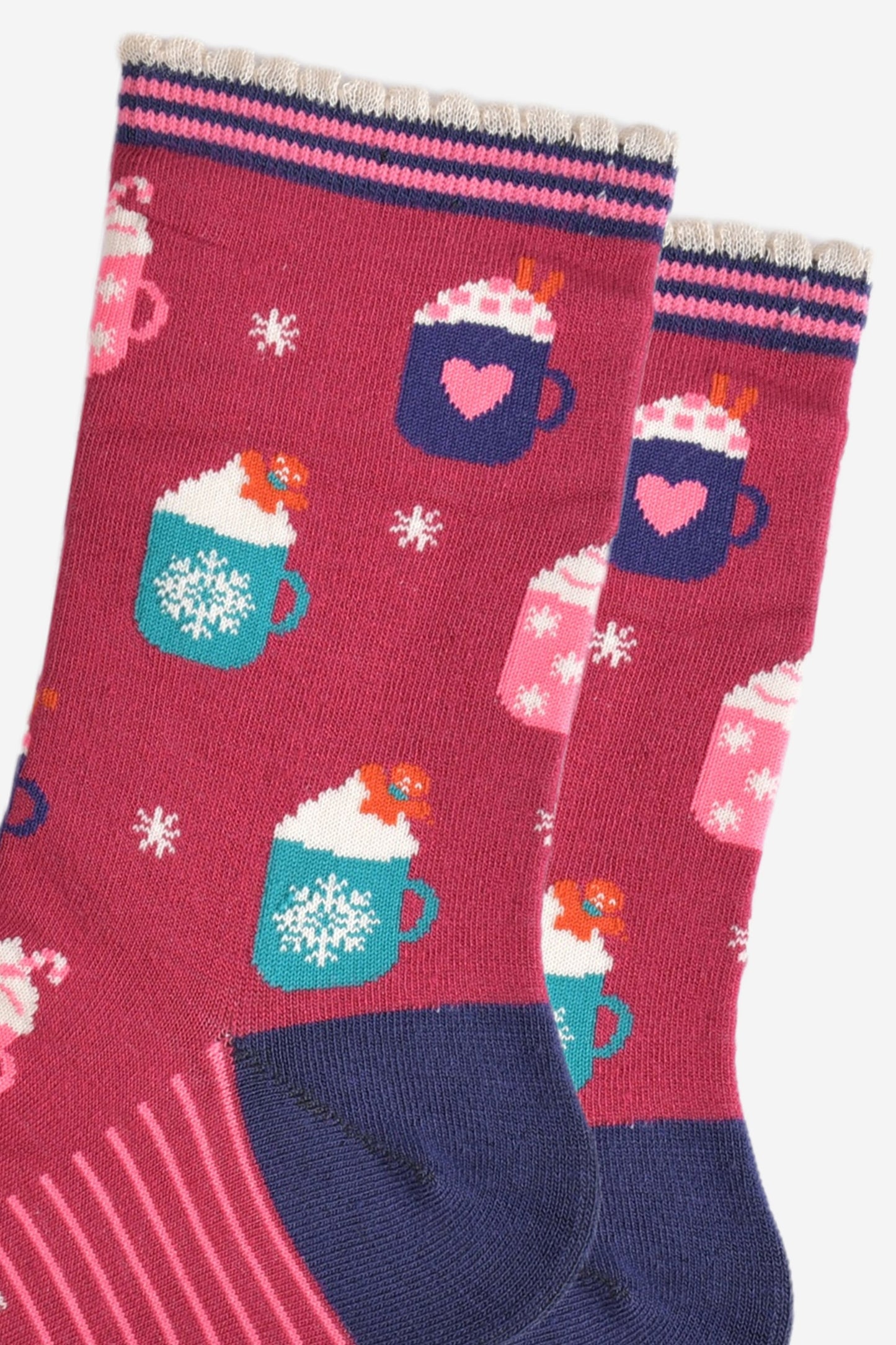 close up of the hot drinks design on the socks, there are teal coloured mugs with a white snowflake pattern topped with whipped creme and a gingerbread man cookie, there are pink mugs with pink candy canes and navy mugs with pink love hearts with pink sugar hearts and cinnamon sticks.