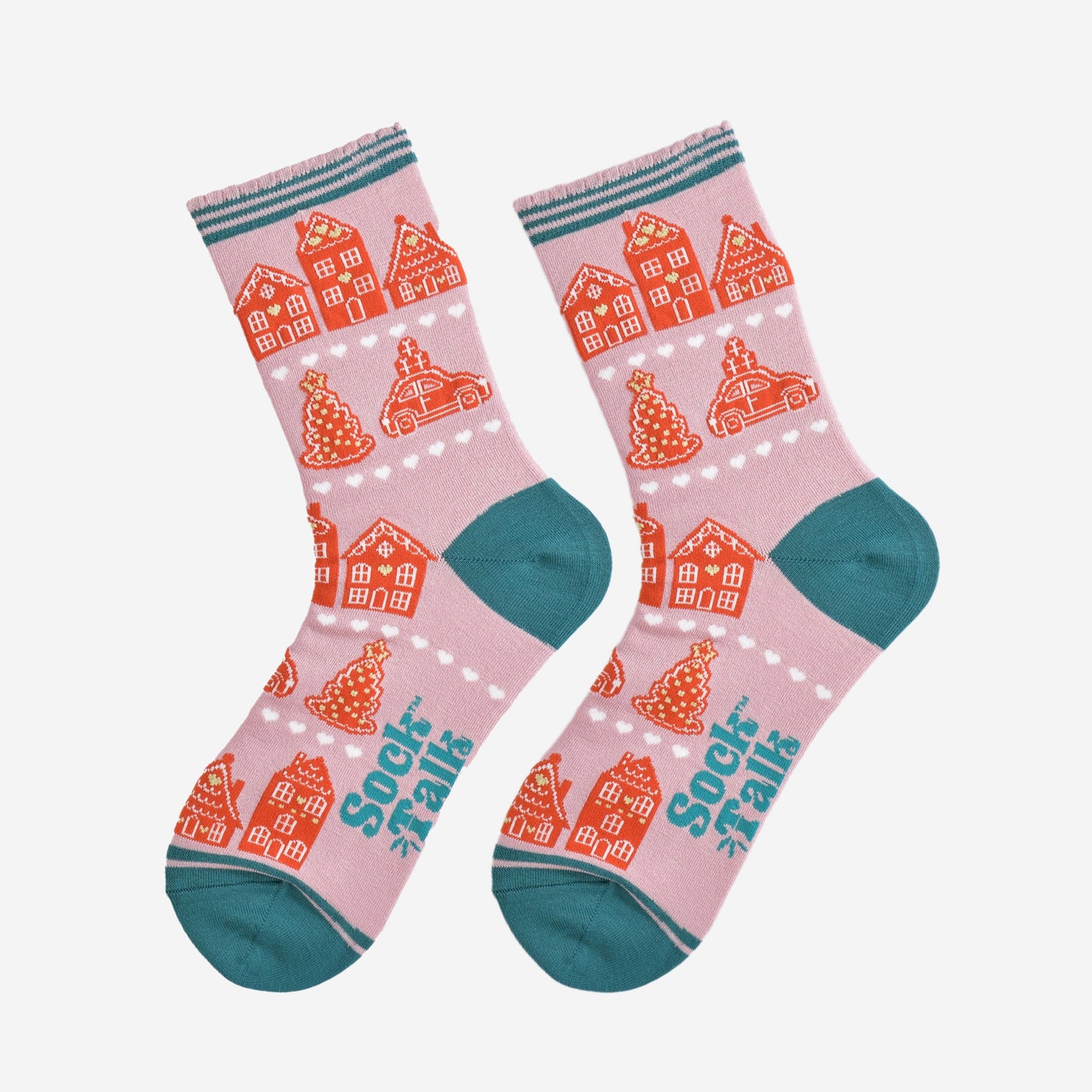 showing the gingerbread house socks laying flat, the pattern is in rows separated by white love heats, the toe and heel of the socks are teal blue in contrast to the light pink background.