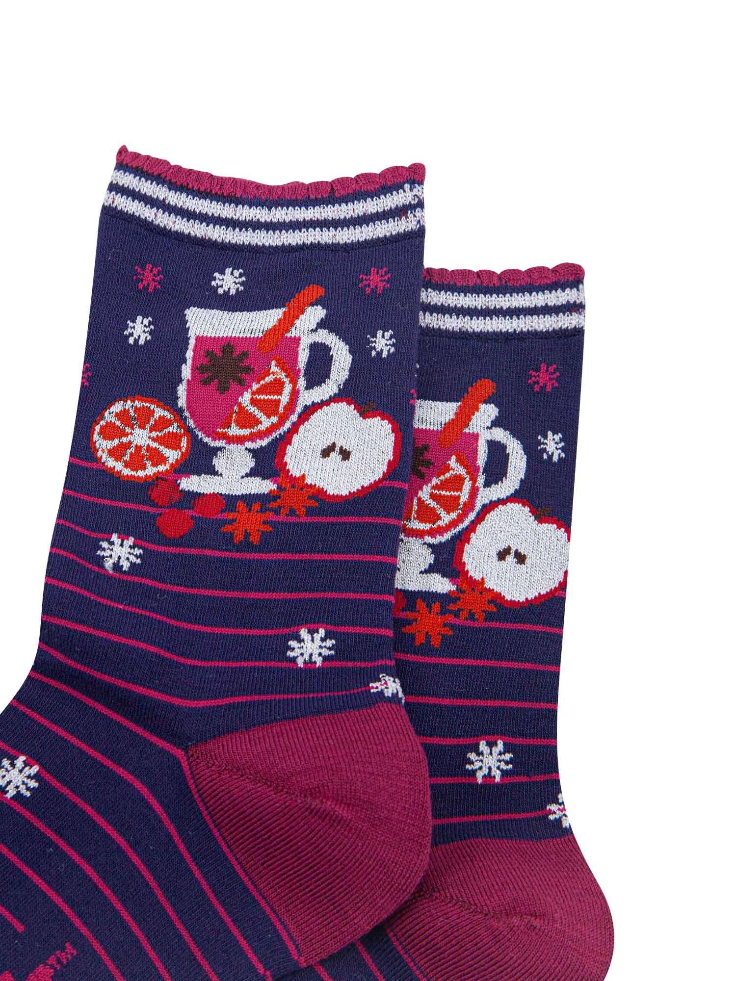 close up of the mulled wine carafe on the ankle of the socks, it is surrounded by orange and apple slices and star anise spice