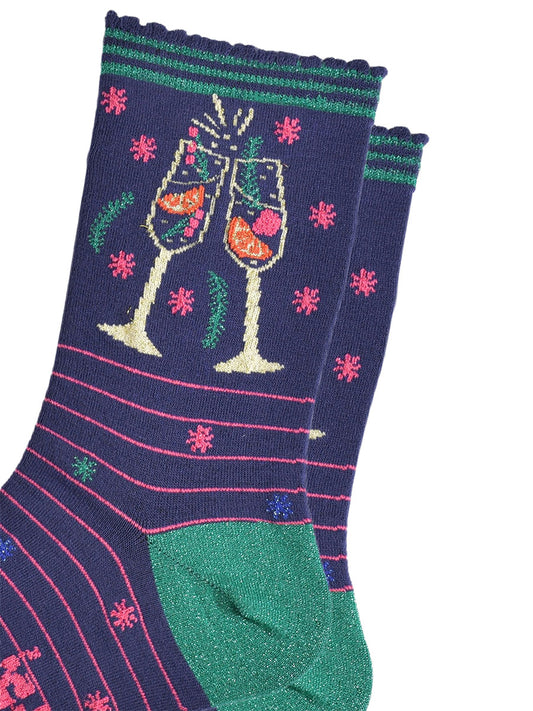close up of the prosecco cocktail glasses on the ankle of the socks, there are orange slices and raspberries inside the glass and it shows sparkling wine. the glasses are clinking in celebration