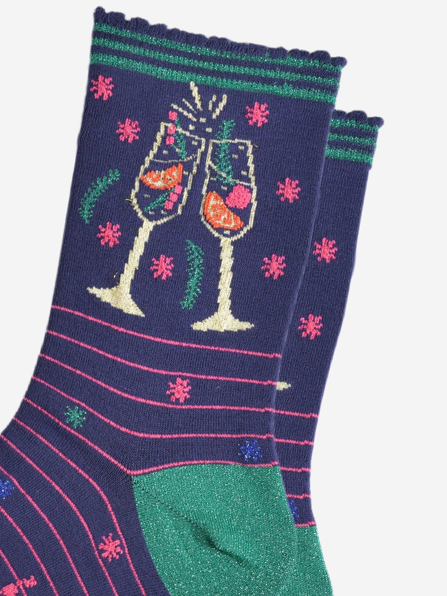 close up of the prosecco cocktail glasses on the ankle of the socks, there are orange slices and raspberries inside the glass and it shows sparkling wine. the glasses are clinking in celebration