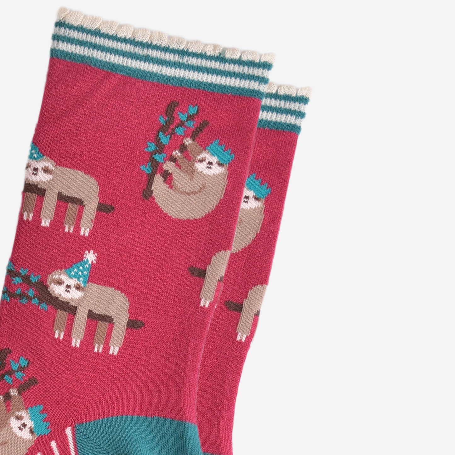 close up of the sloth pattern on the socks, there are sloths laying flat on a branch with their limbs dangling, these are wearing green party hats, there also sloths climbing branches, these are wearing festive crown party hats