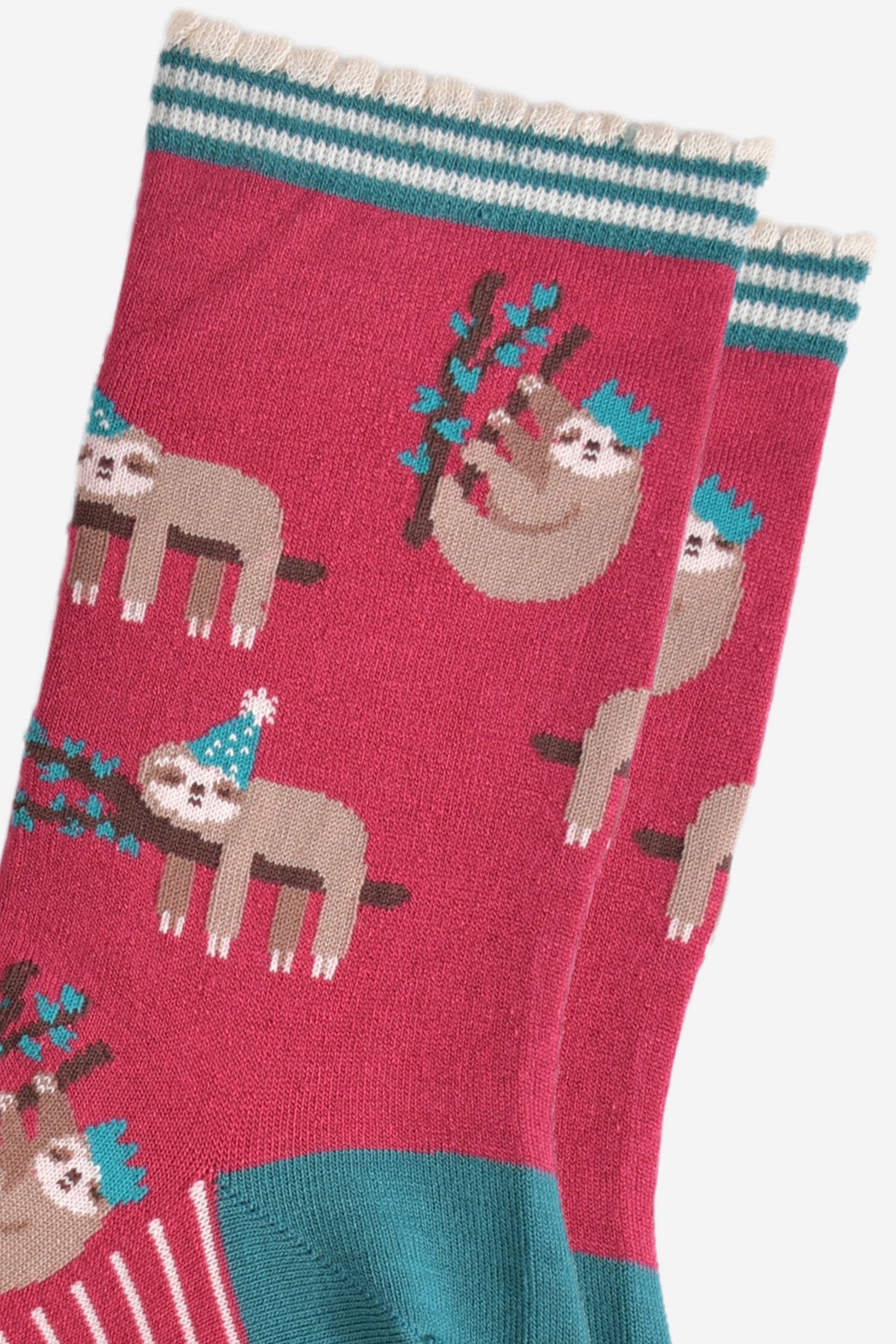 close up of the sloth pattern on the socks, there are sloths laying flat on a branch with their limbs dangling, these are wearing green party hats, there also sloths climbing branches, these are wearing festive crown party hats