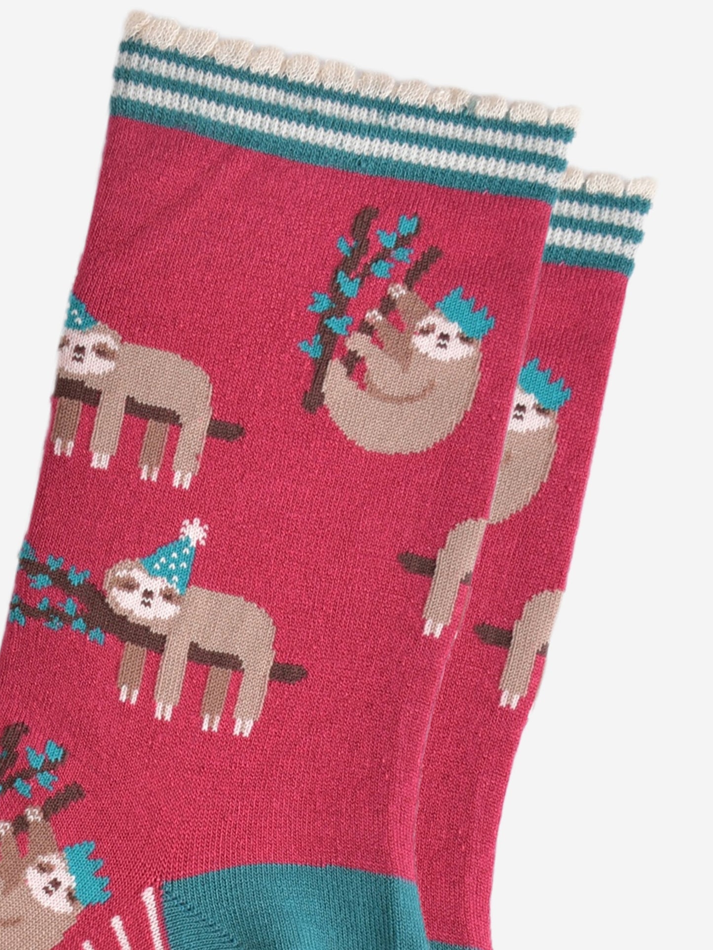 close up of the sloth pattern on the socks, there are sloths laying flat on a branch with their limbs dangling, these are wearing green party hats, there also sloths climbing branches, these are wearing festive crown party hats