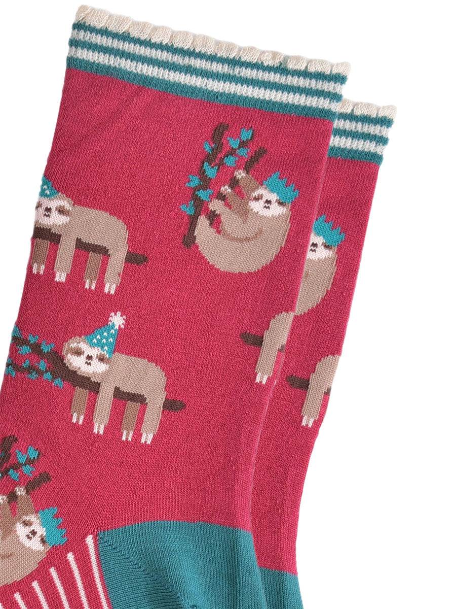 close up of the sloth pattern on the socks, there are sloths laying flat on a branch with their limbs dangling, these are wearing green party hats, there also sloths climbing branches, these are wearing festive crown party hats