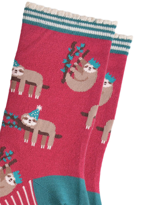close up of the sloth pattern on the socks, there are sloths laying flat on a branch with their limbs dangling, these are wearing green party hats, there also sloths climbing branches, these are wearing festive crown party hats