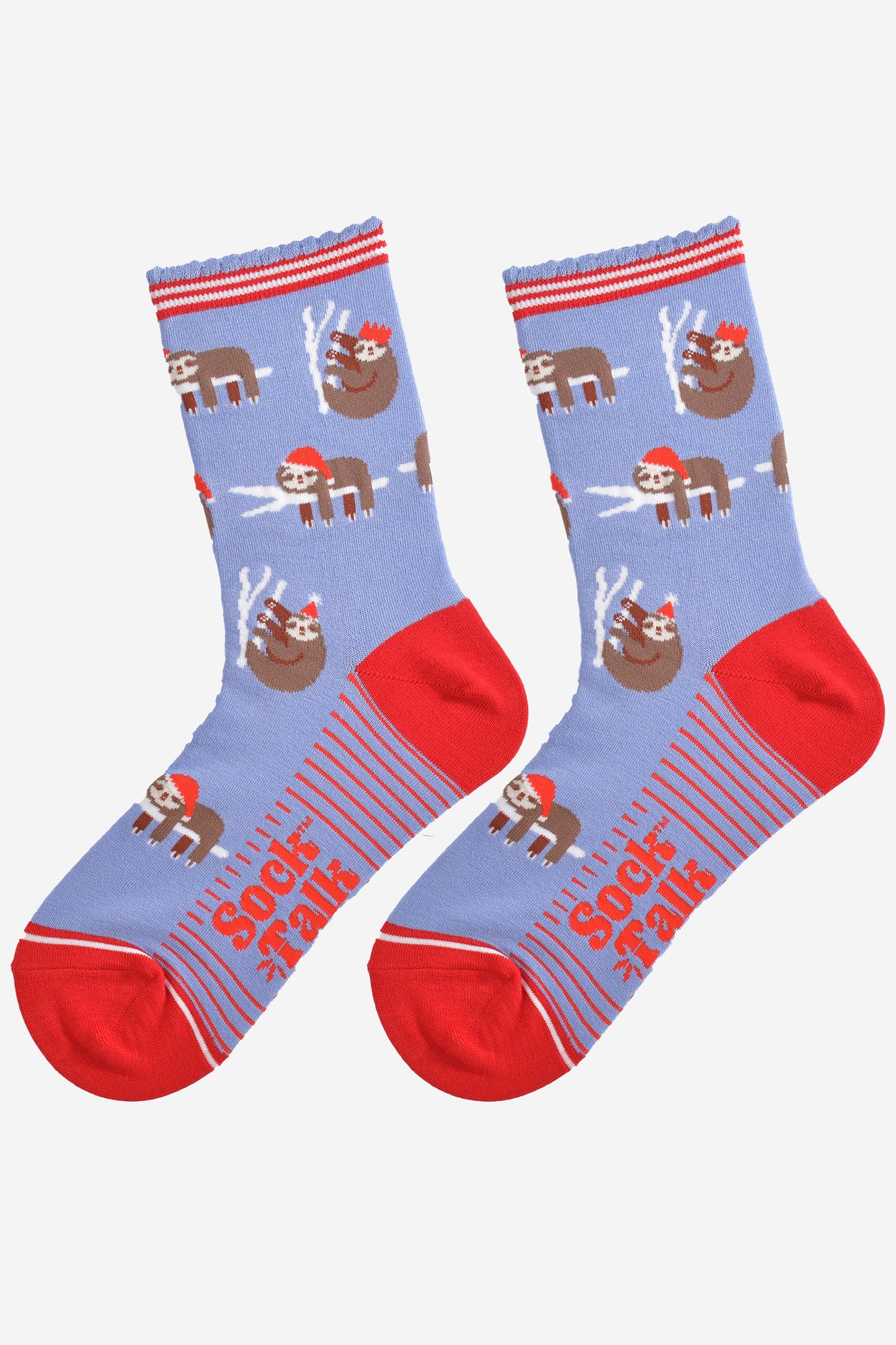 showing the festive sloth socks laying flat displaying the full pattern, there are sloths laying and climbing on tree branches while wearing santa hats and party hats, the sole of the socs have a red striped pattern