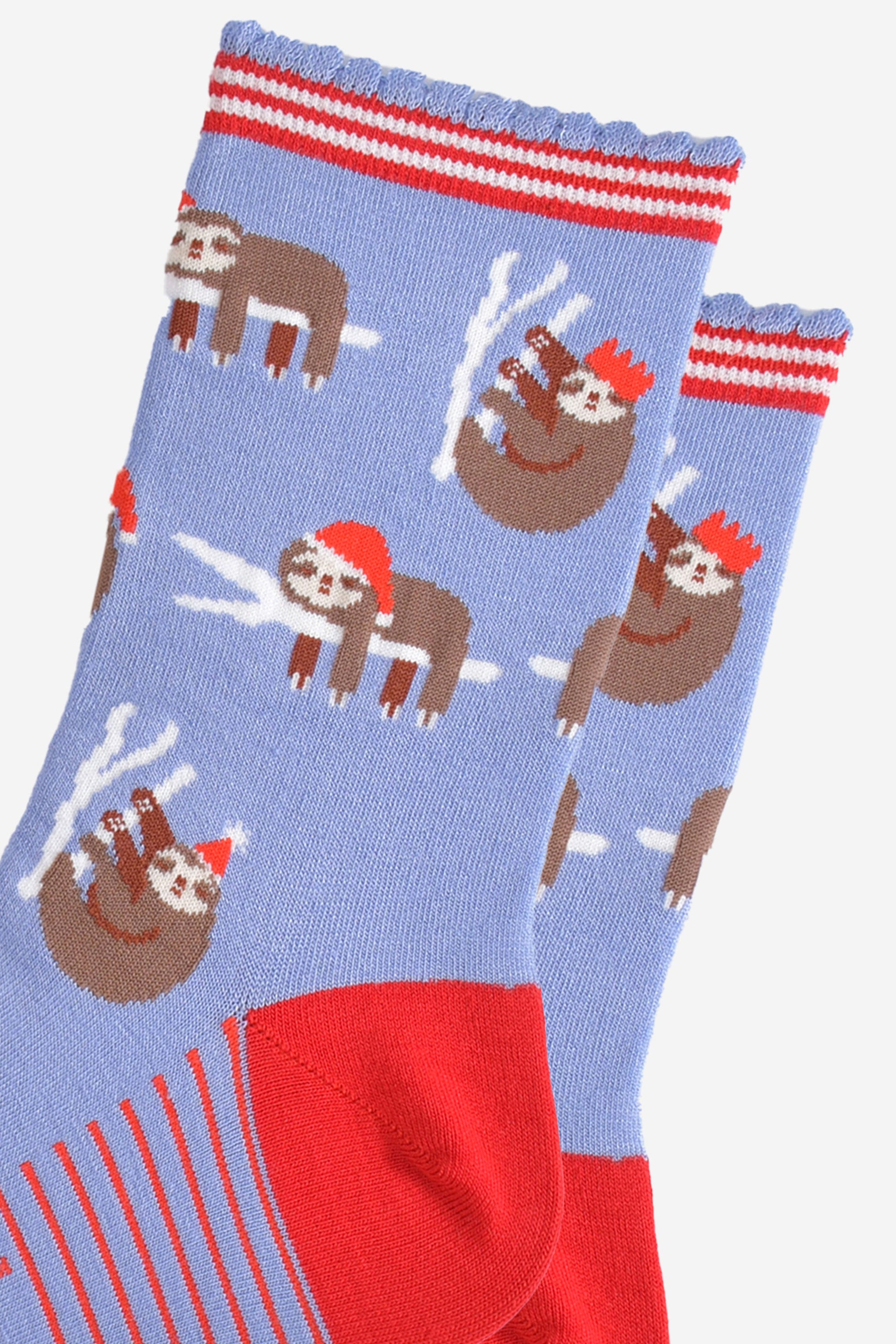 close up of the sloth pattern on the socks, there are sloths laying flat on a branch with their limbs dangling, these are wearing santa hats, there also sloths climbing branches, these are wearing festive party hats