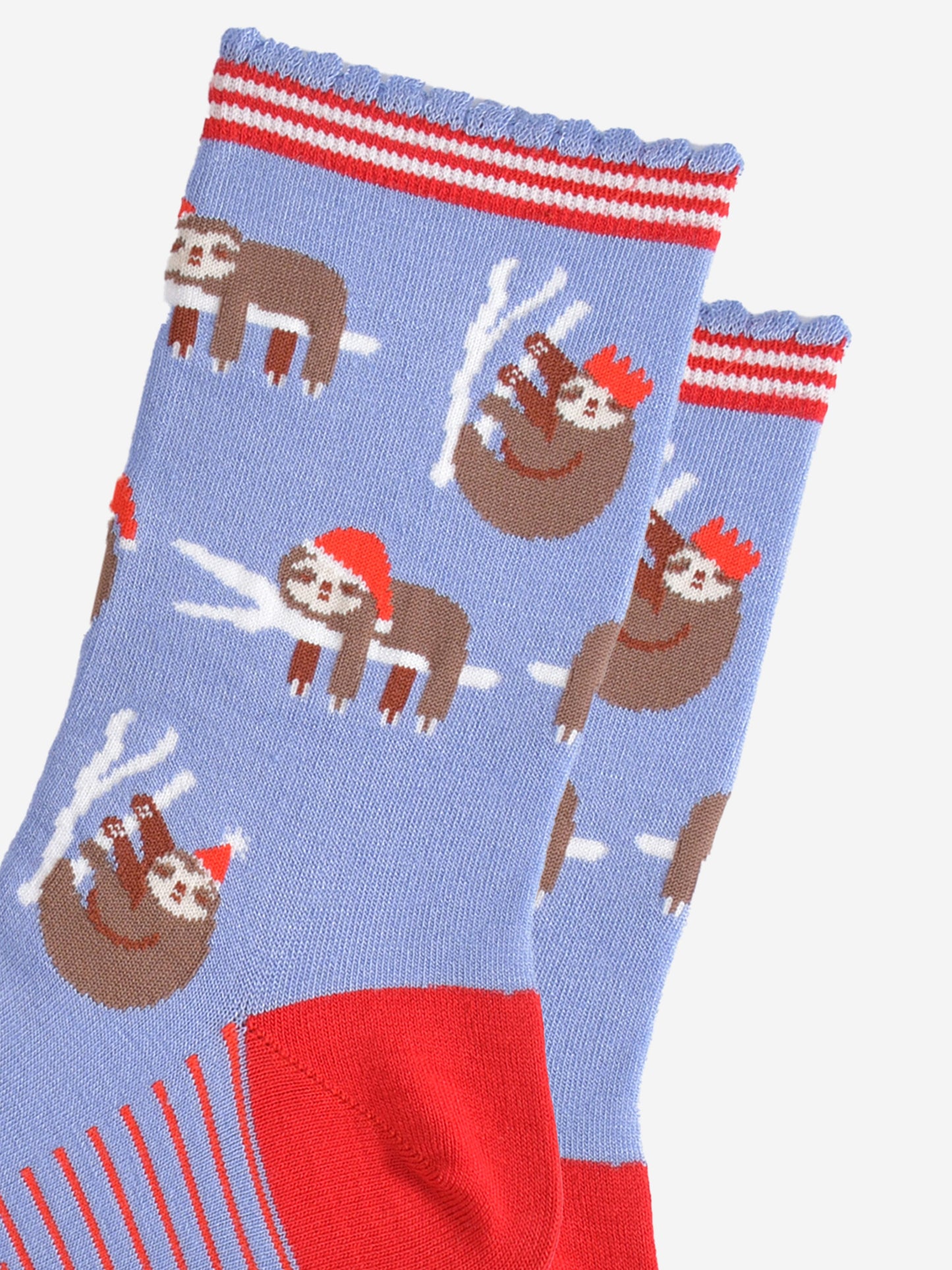 close up of the sloth pattern on the socks, there are sloths laying flat on a branch with their limbs dangling, these are wearing santa hats, there also sloths climbing branches, these are wearing festive party hats