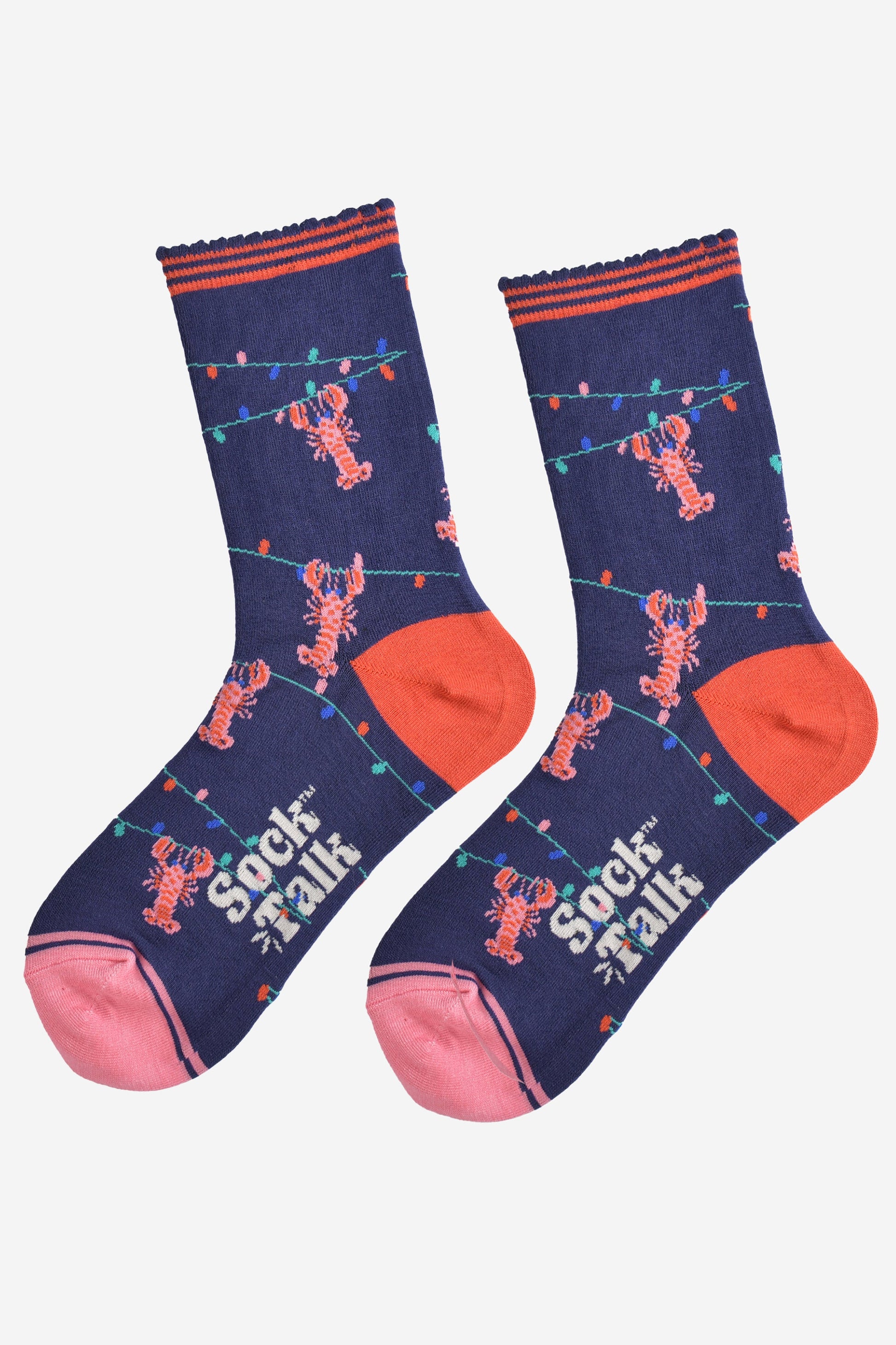 showing the lobster socks laying flat highlighting the all over pattern of the colourful party lights with pink lobsters hanging from them, the toe is pink and the heel is coral in contrast to the navy blue of the socks