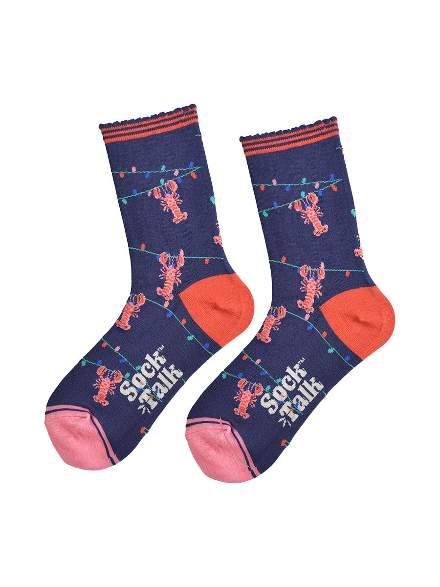showing the lobster socks laying flat highlighting the all over pattern of the colourful party lights with pink lobsters hanging from them, the toe is pink and the heel is coral in contrast to the navy blue of the socks
