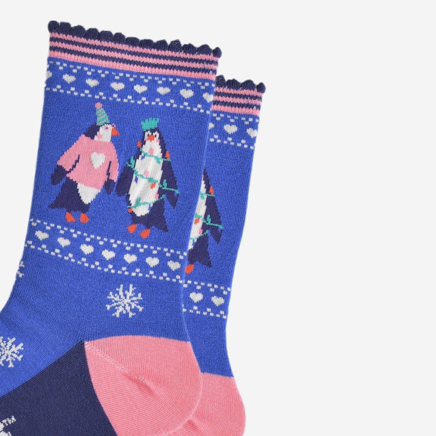 close up of the penguins on the ankle of the socks, one is wearing a pink xmas jumper and green party hat. the other penguin is entangled in festive party lights and is also wearing a crown shaped party hat