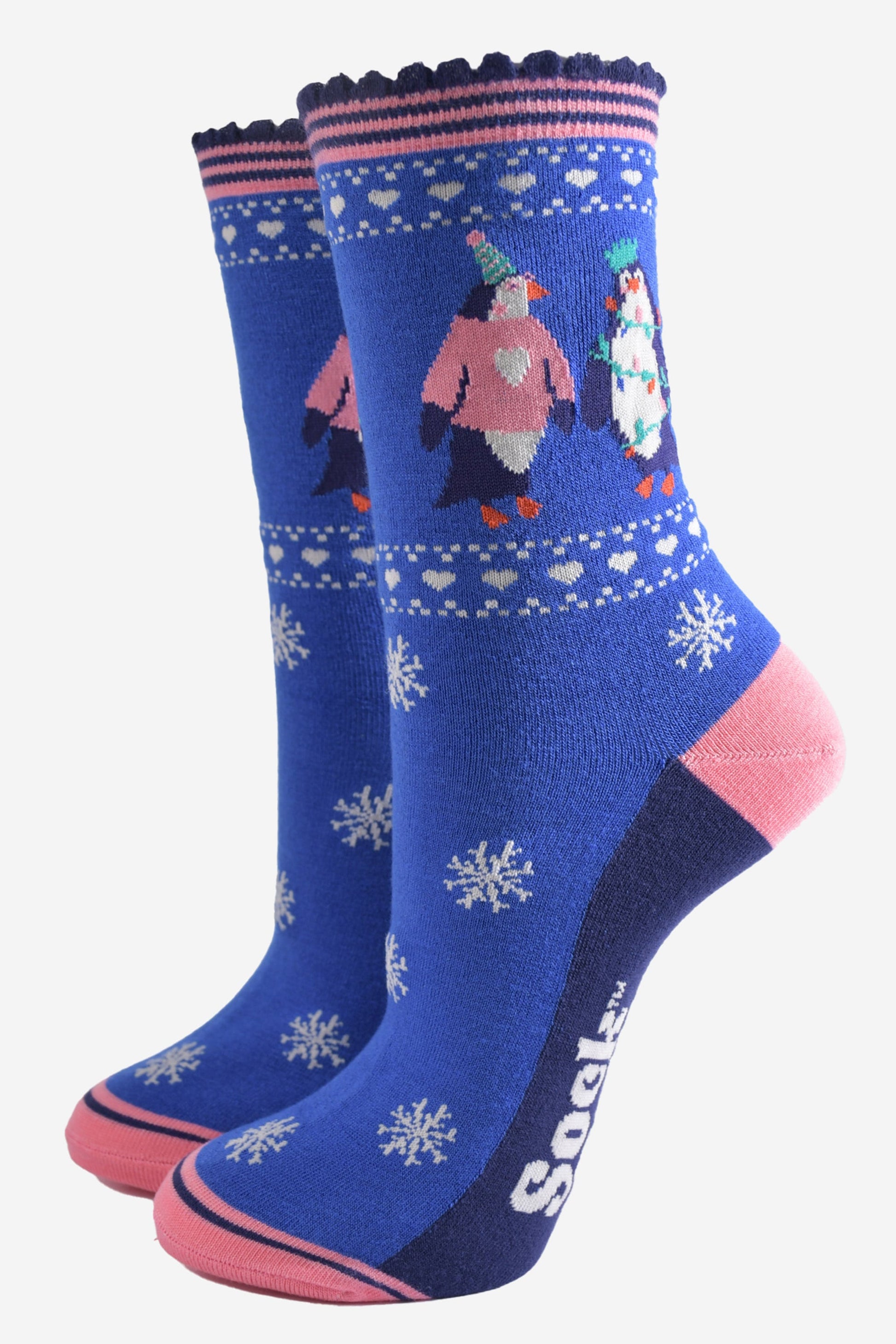 blue socks with pink accents and white snow flakes with a penguins on the ankle, the penguins are wearing party hats, xmas jumpers and christmas party lights