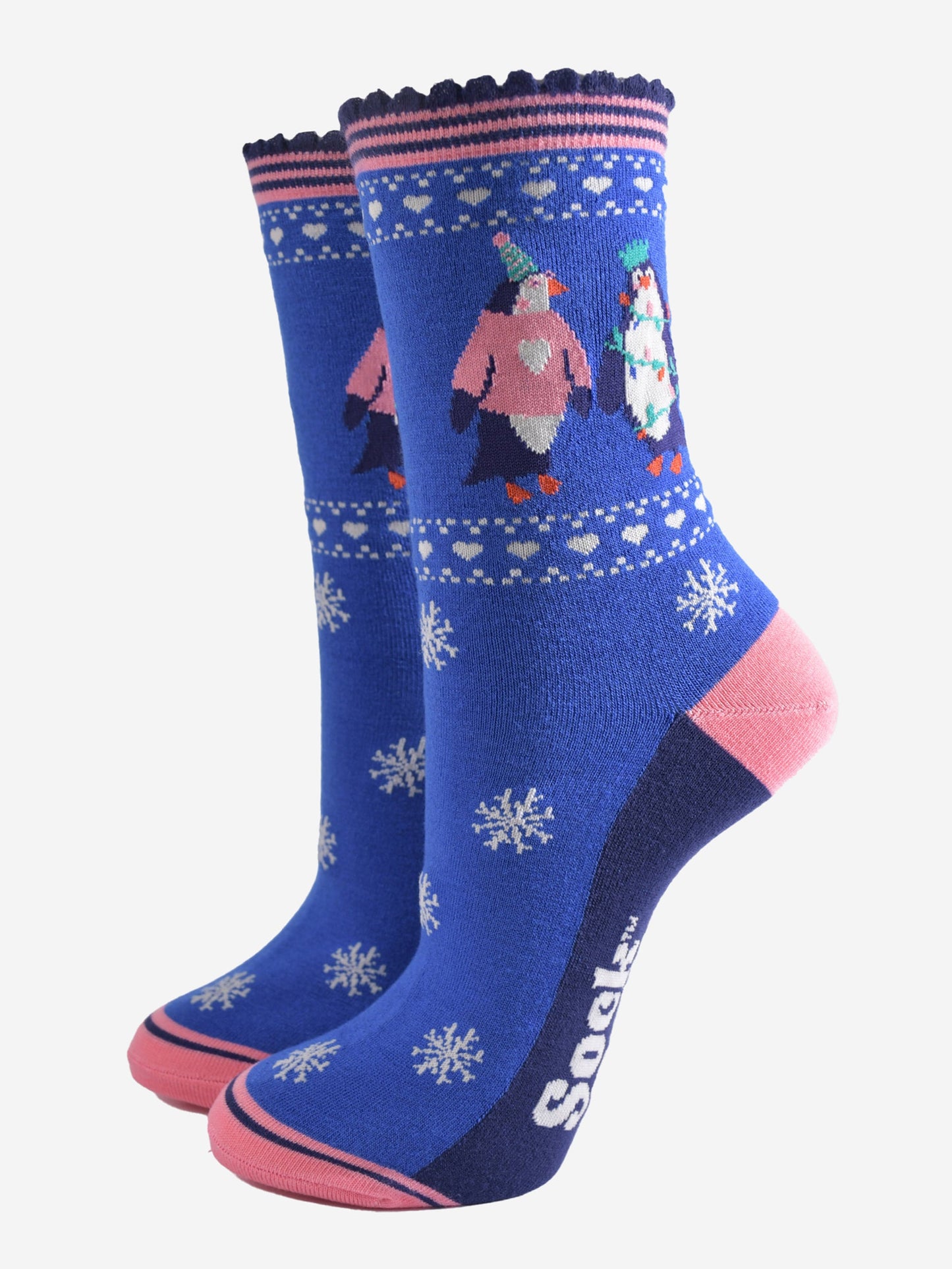 blue socks with pink accents and white snow flakes with a penguins on the ankle, the penguins are wearing party hats, xmas jumpers and christmas party lights