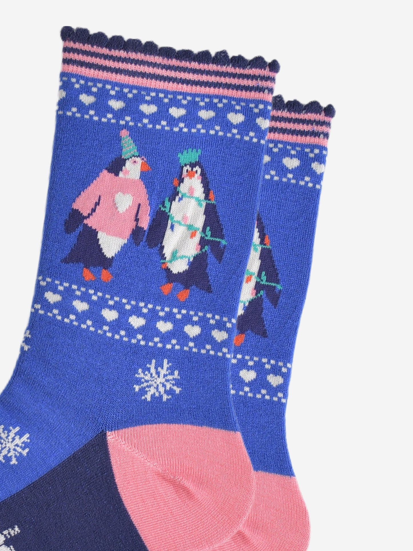 close up of the penguins on the ankle of the socks, one is wearing a pink xmas jumper and green party hat. the other penguin is entangled in festive party lights and is also wearing a crown shaped party hat