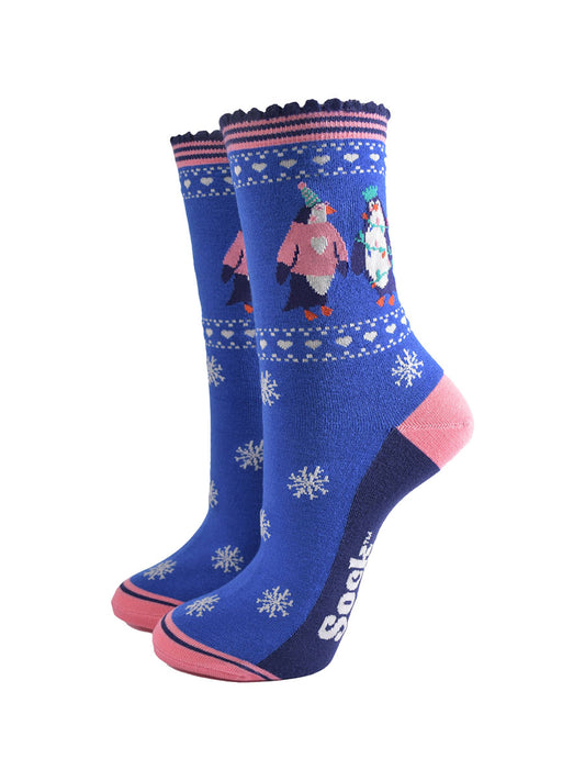 blue socks with pink accents and white snow flakes with a penguins on the ankle, the penguins are wearing party hats, xmas jumpers and christmas party lights