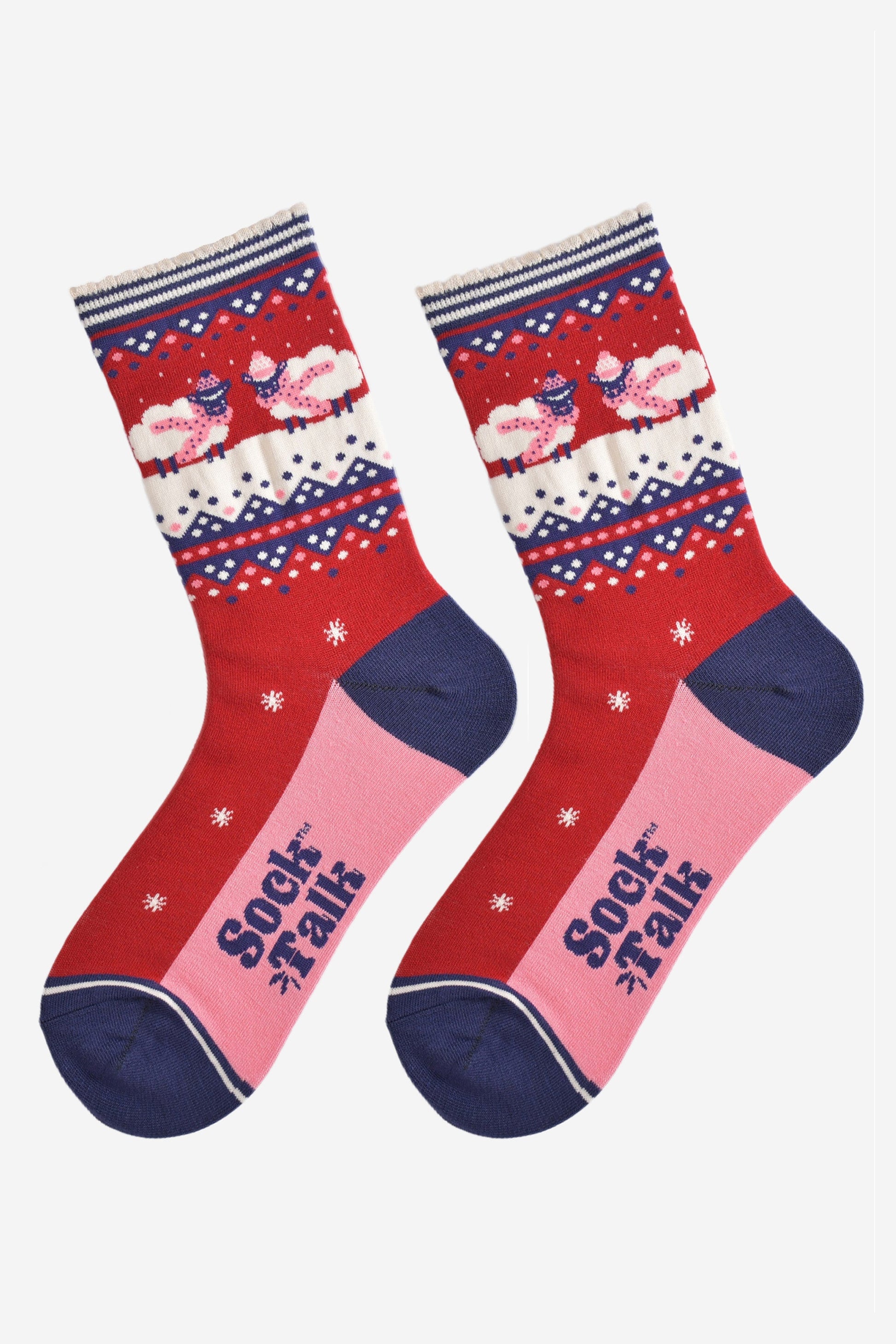 showing the socks laying flat, they have a pink sole and navy blue toe and heel in contrast to the red base of the socks. on the ankles there are sheep standing in a snowy field while wearing pink winter hats and scarves