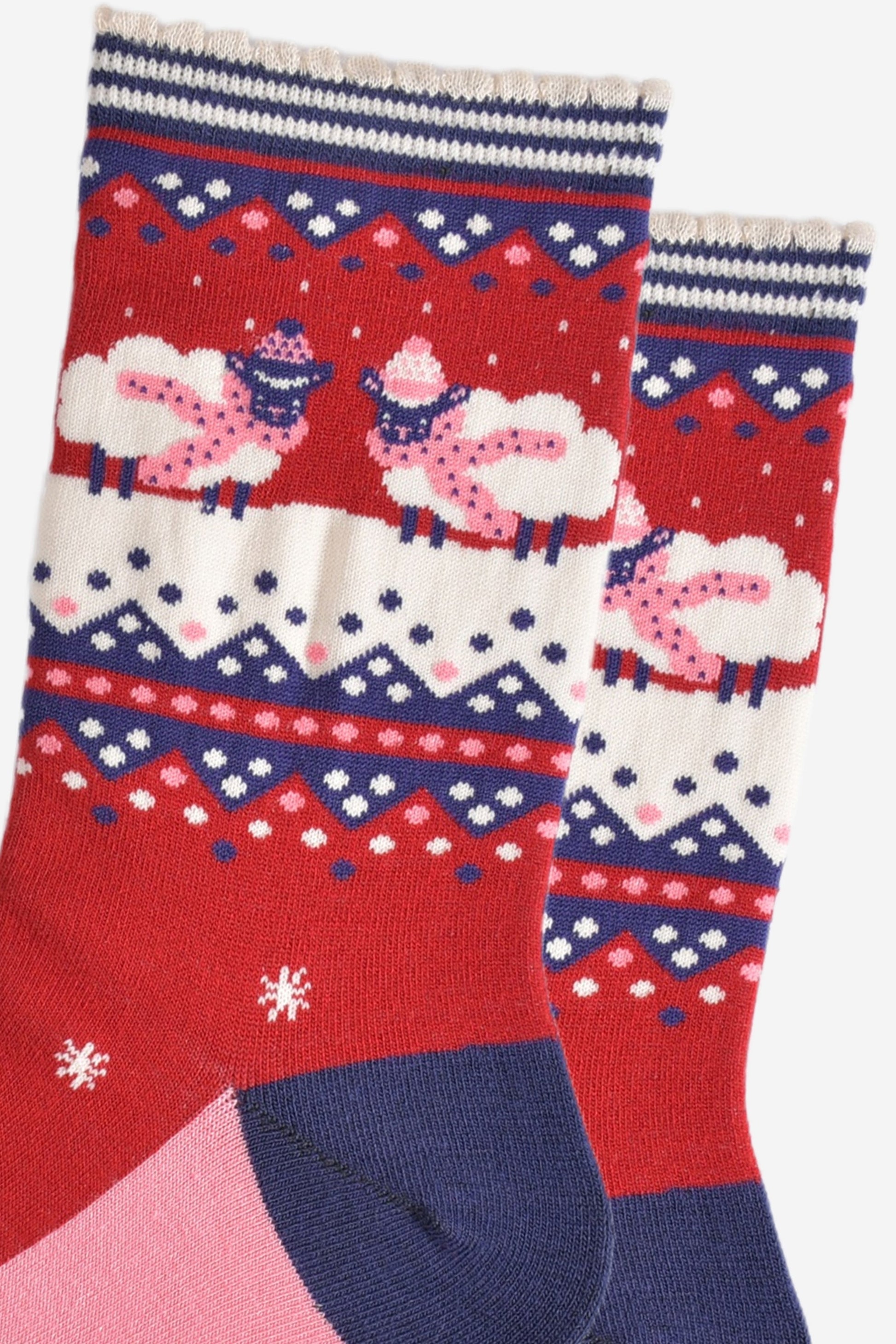 close up of the sheep pattern on the ankles of the socks, they are standing knee deep in snow and they are both wearing pink scarves and winter hats