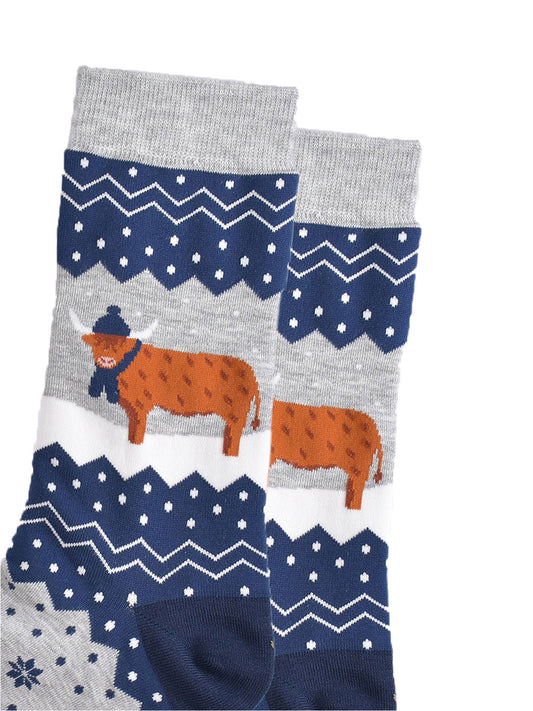 close up of the highland cow, it is standing in the snow and wearing a winter hat and scarf