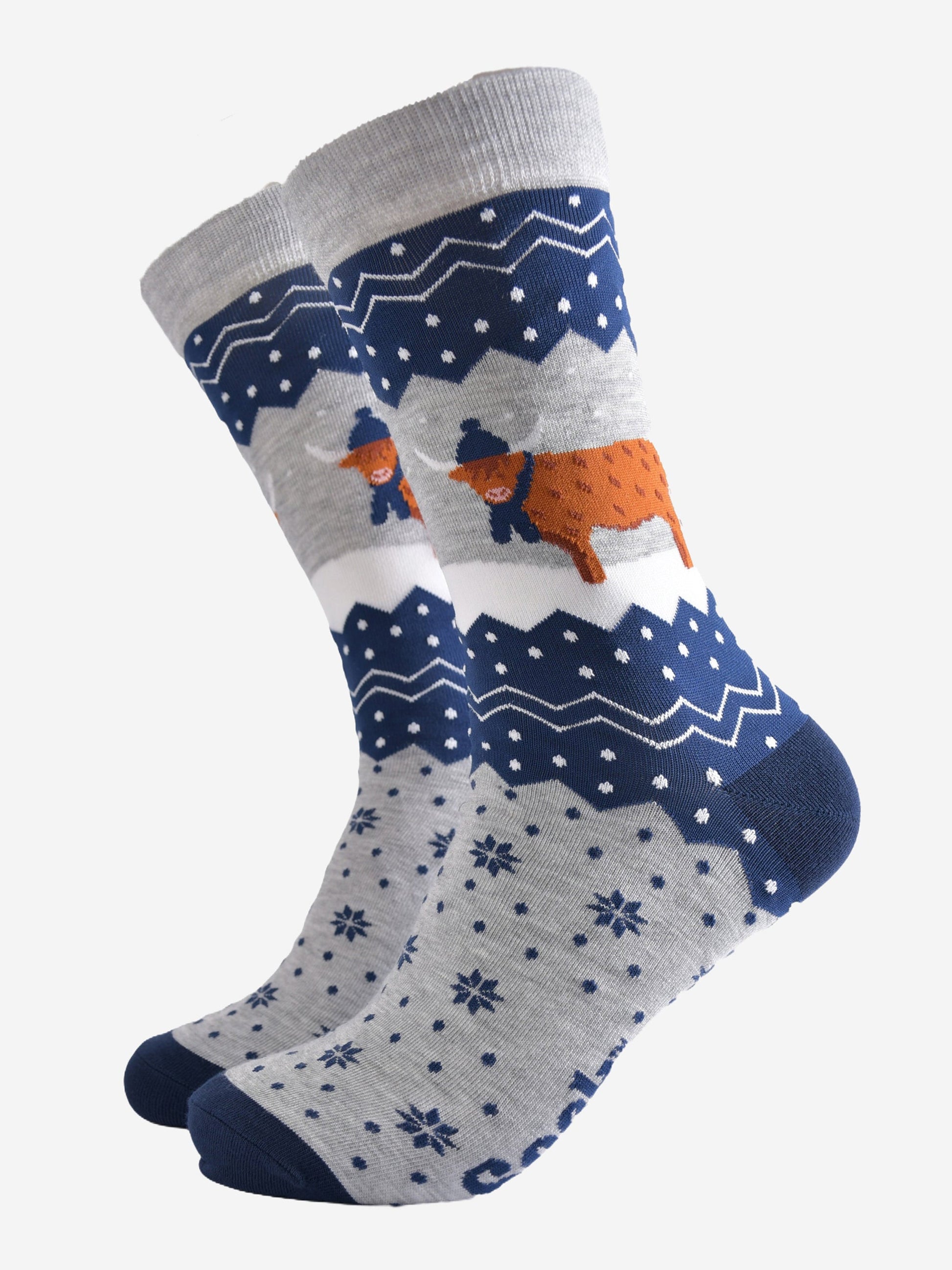 navy blue and grey bamboo socks with a fair isle zig zag and snowflake pattern, featuring a highland cow standing in a snowy field wearing a blue winter hat