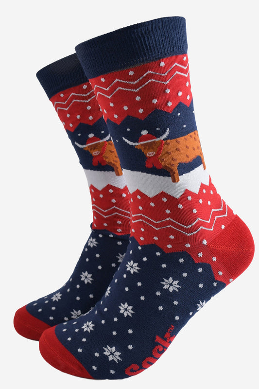 navy blue and red bamboo socks with a fair isle zig zag and snowflake pattern, featuring a highland cow standing in a snowy field wearing a santa hat