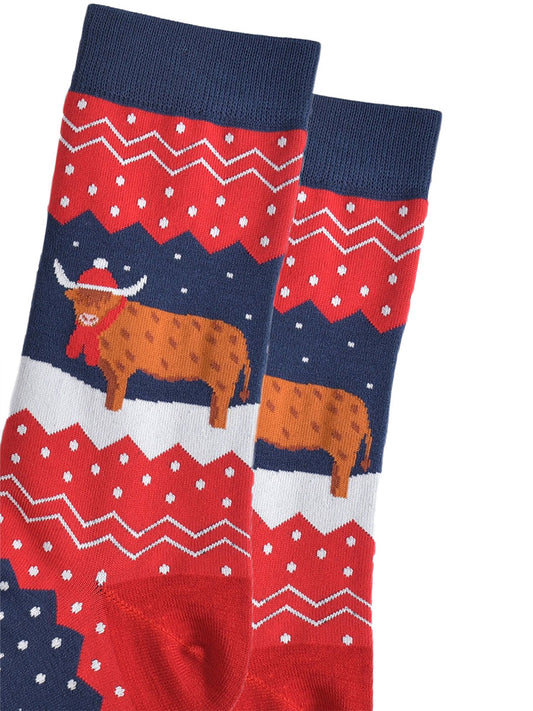 close up of the highland cow, it is standing in the snow and wearing a santa hat and winter scarf