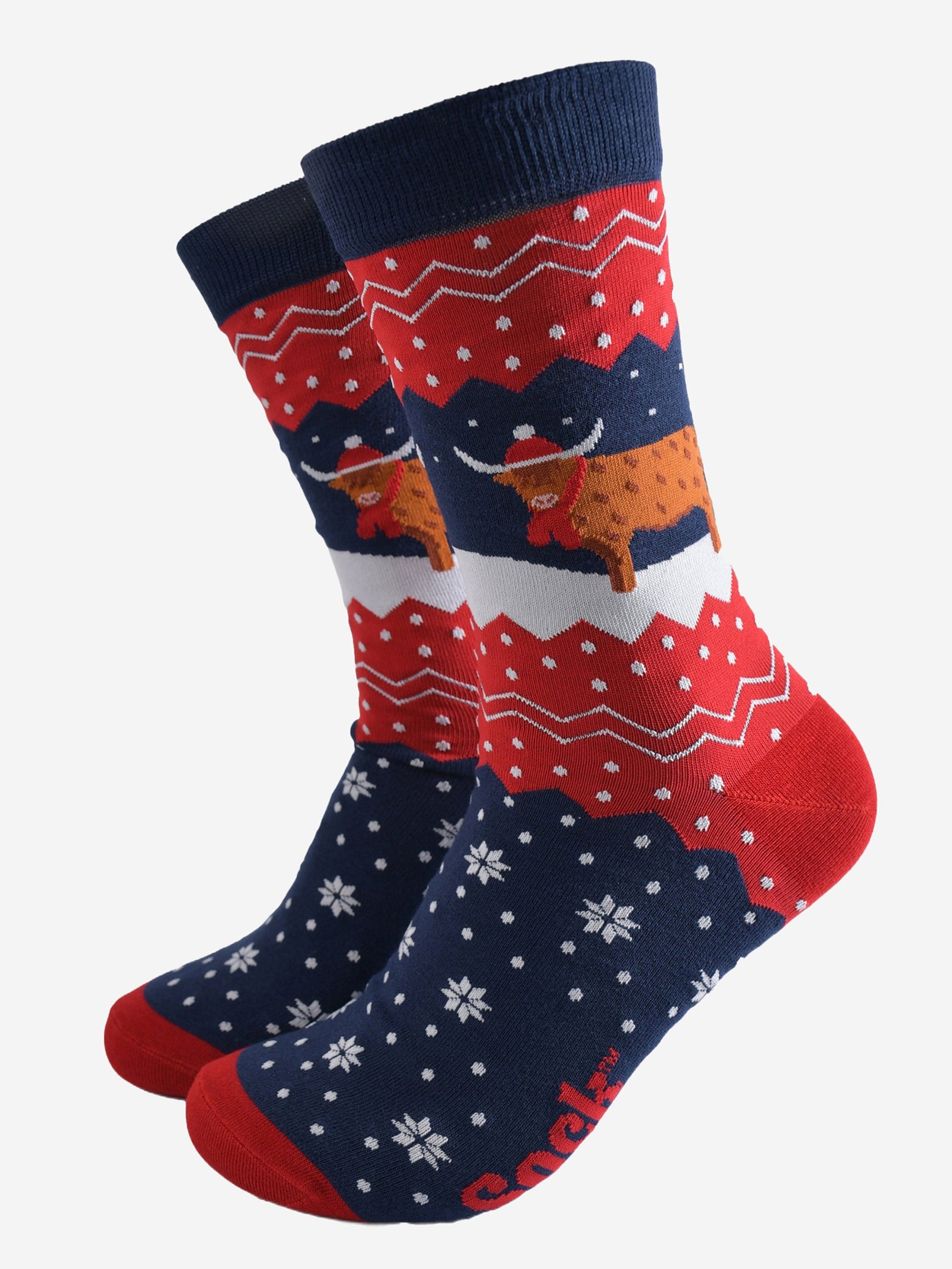 navy blue and red bamboo socks with a fair isle zig zag and snowflake pattern, featuring a highland cow standing in a snowy field wearing a santa hat